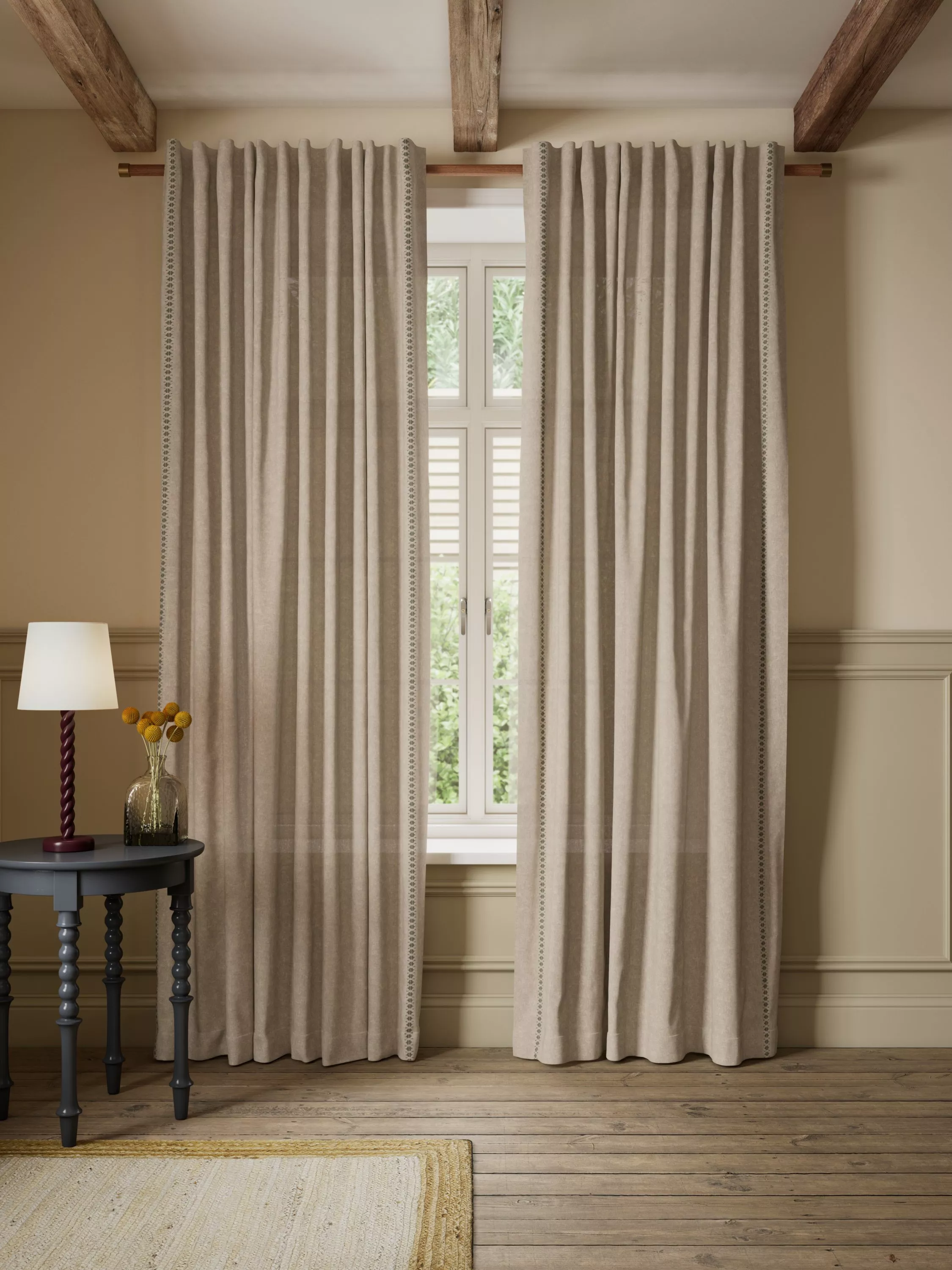 Neutral linen curtains framing a white window in a rustic room with wooden beams and side table lamp.