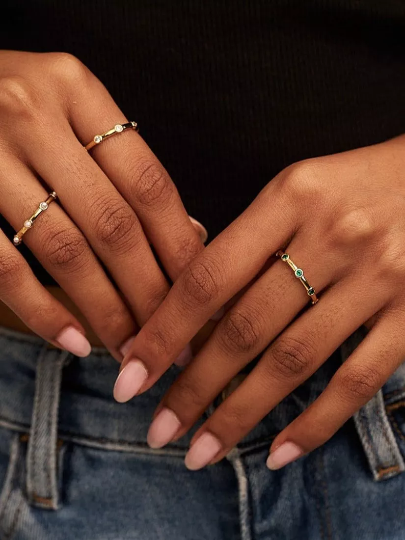 Hand with 3 gold rings stack on one finger and a gold bracelet, with pink nail varnish