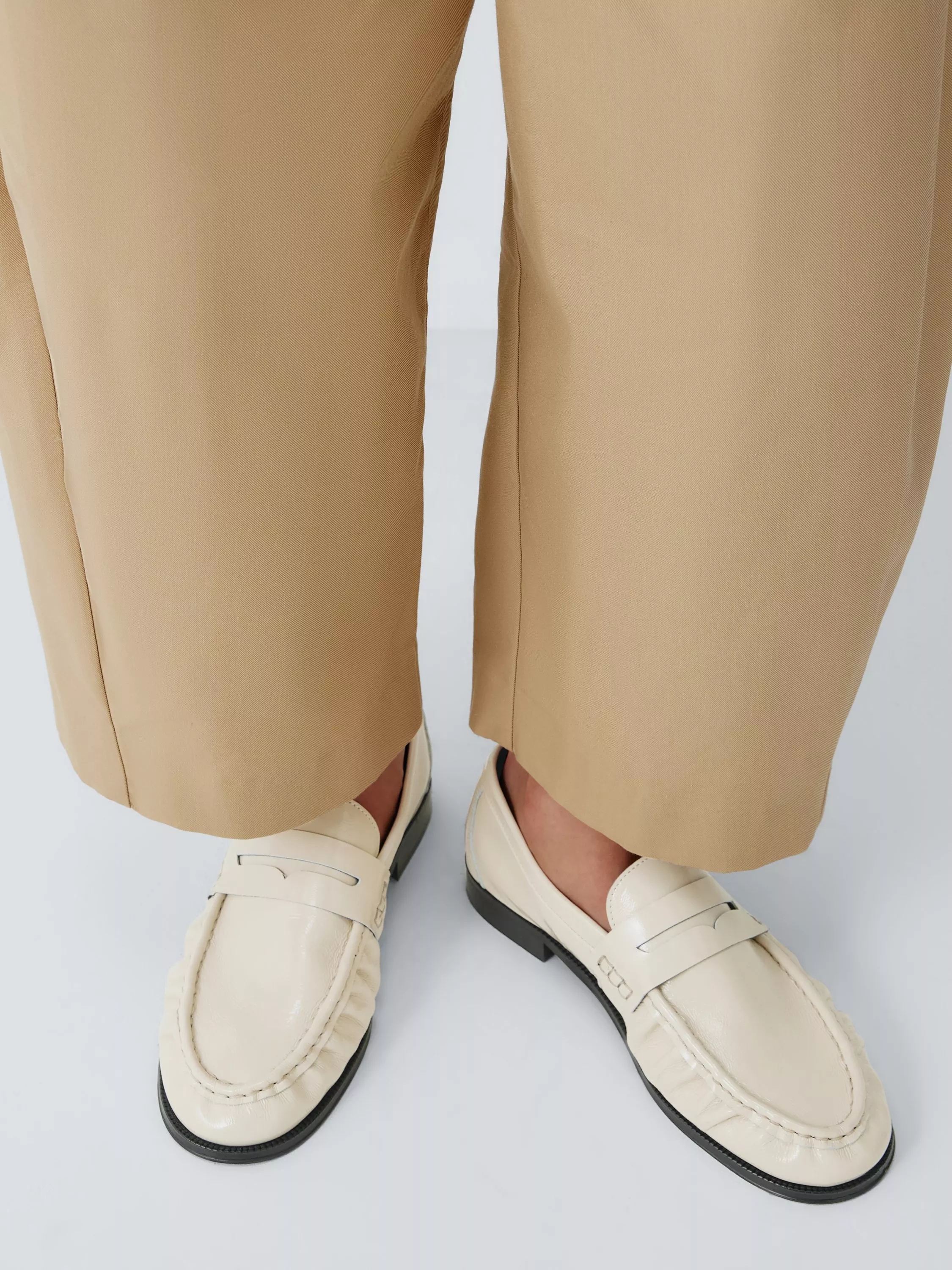 Close-up of beige tailored trousers with cream leather loafers, smart casual outfit detail on studio background