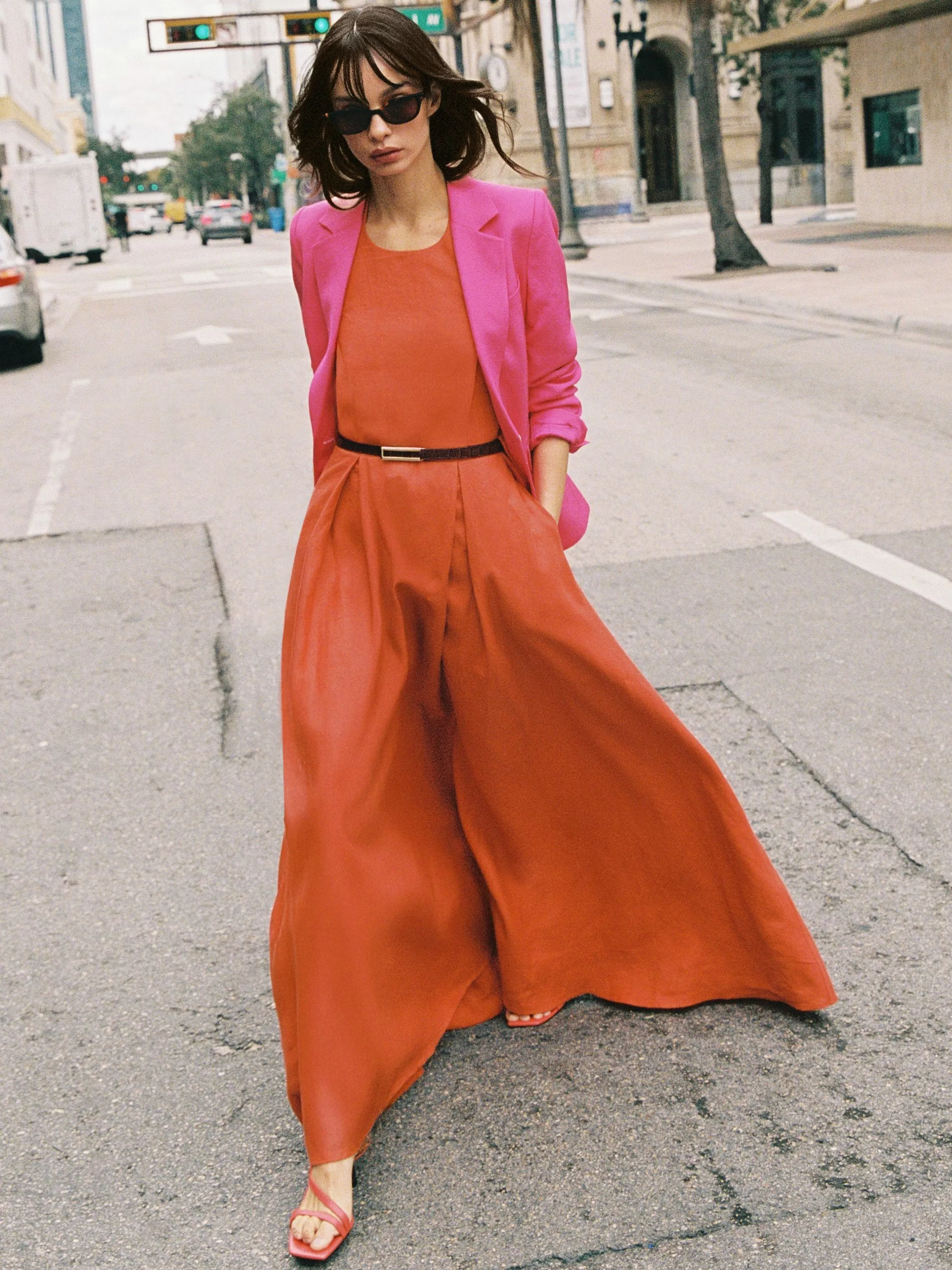A stylish woman in a grey blazer and blue trousers, sitting confidently on a stone seat. Fashionable and poised.