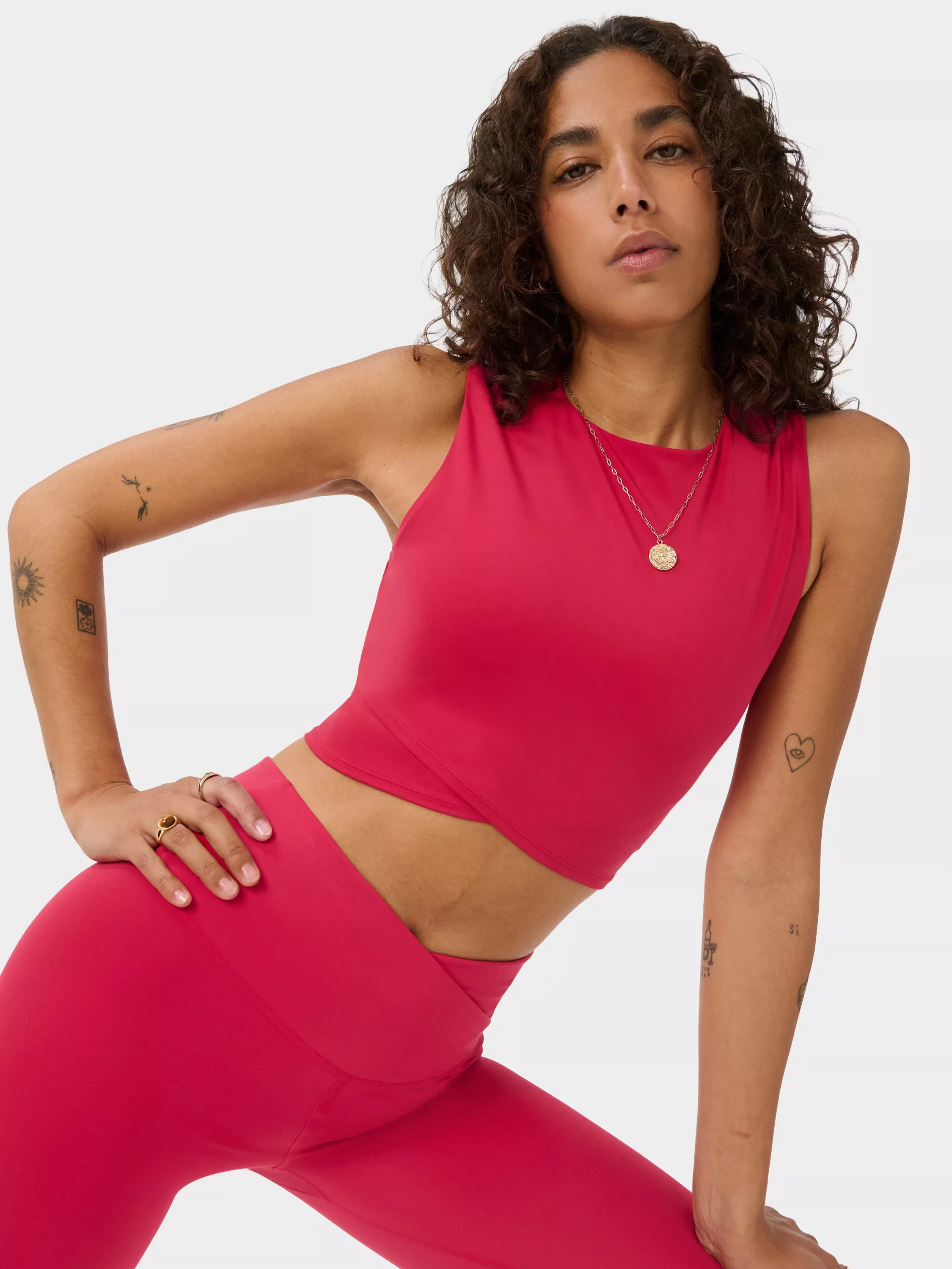 Model wearing bright pink sleeveless activewear crop top and high-waisted leggings, studio fitness fashion close-up.