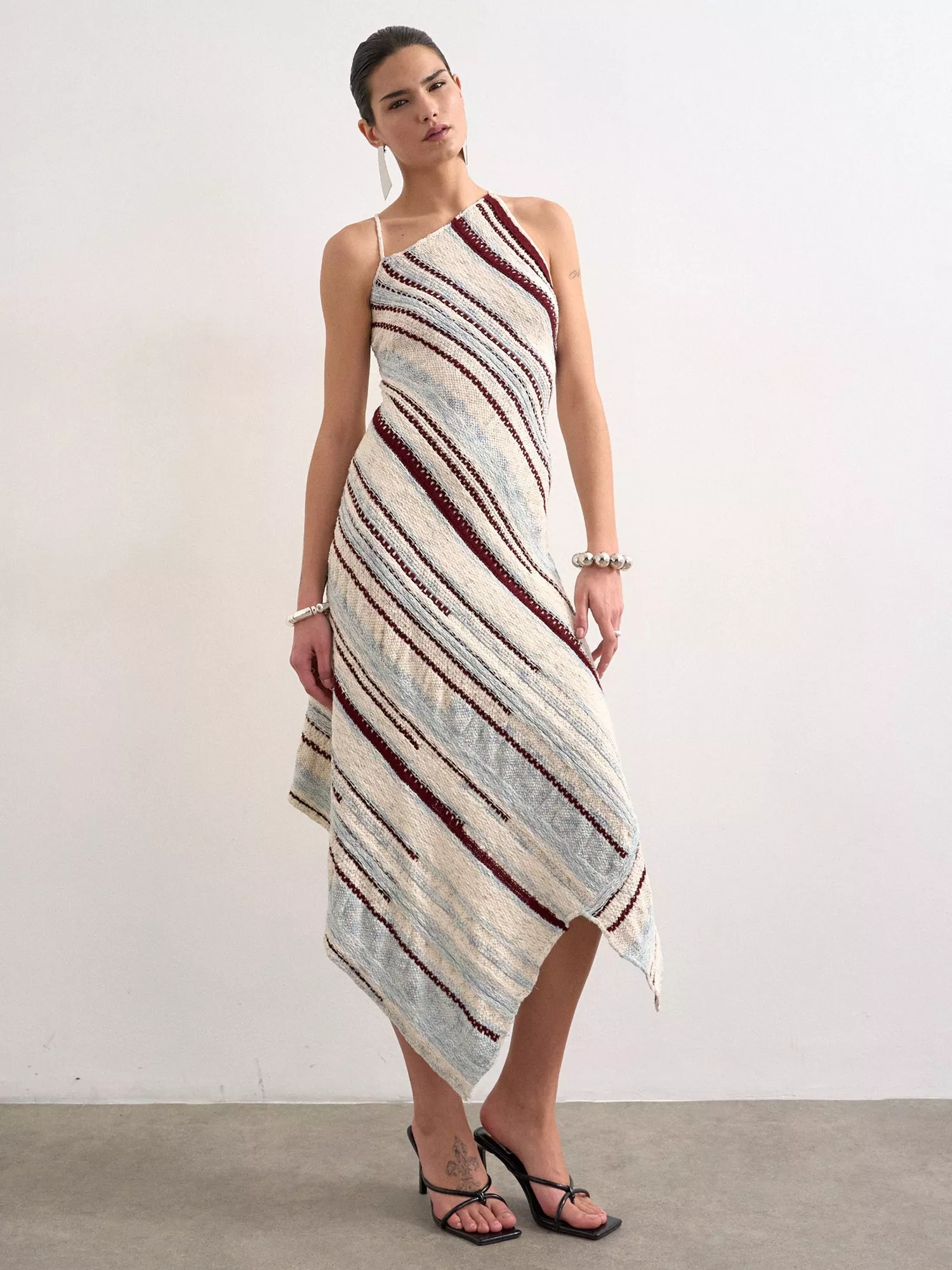 Model wearing an asymmetrical striped one-shoulder midi dress with handkerchief hem, styled with heels.