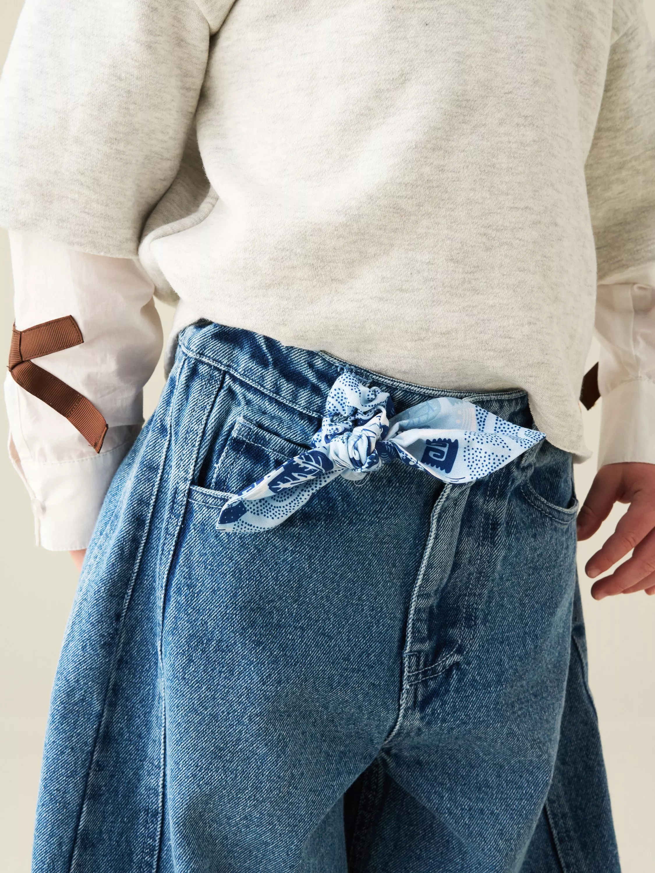 Close-up of denim apron trousers with blue bandana tie, worn with layered jumper and shirt sleeves