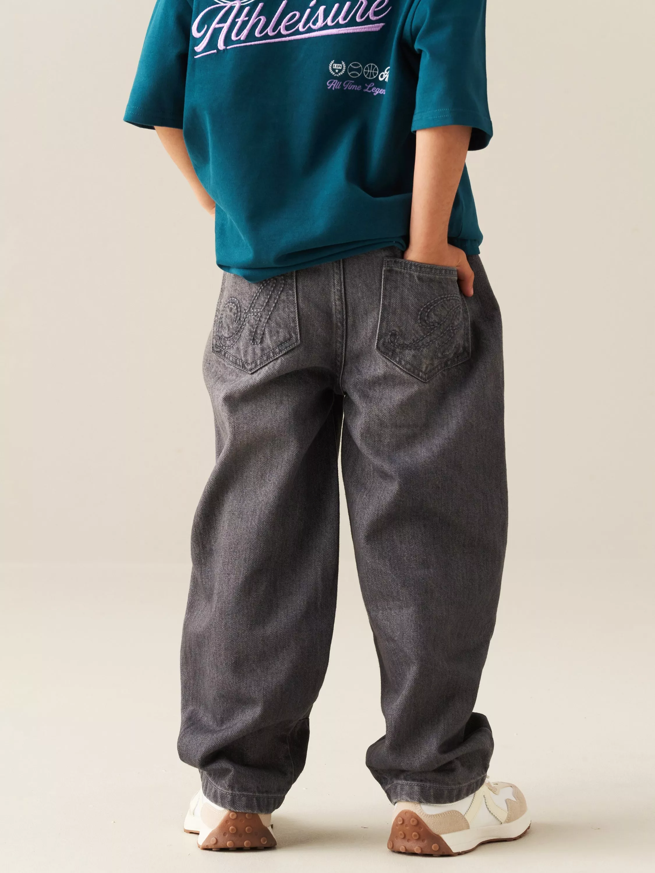 Close-up of grey wide-leg cargo jeans with side seams, worn with navy jacket and white trainers, casual outfit
