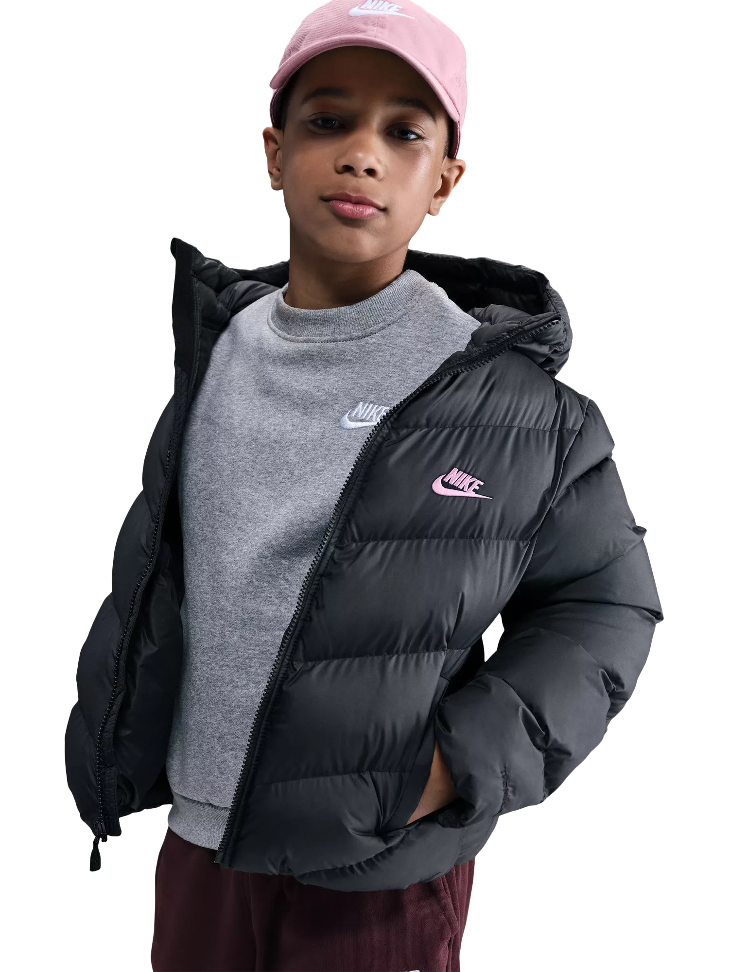 Boy in black Nike puffer jacket, grey sweatshirt and pink cap, studio portrait on white background