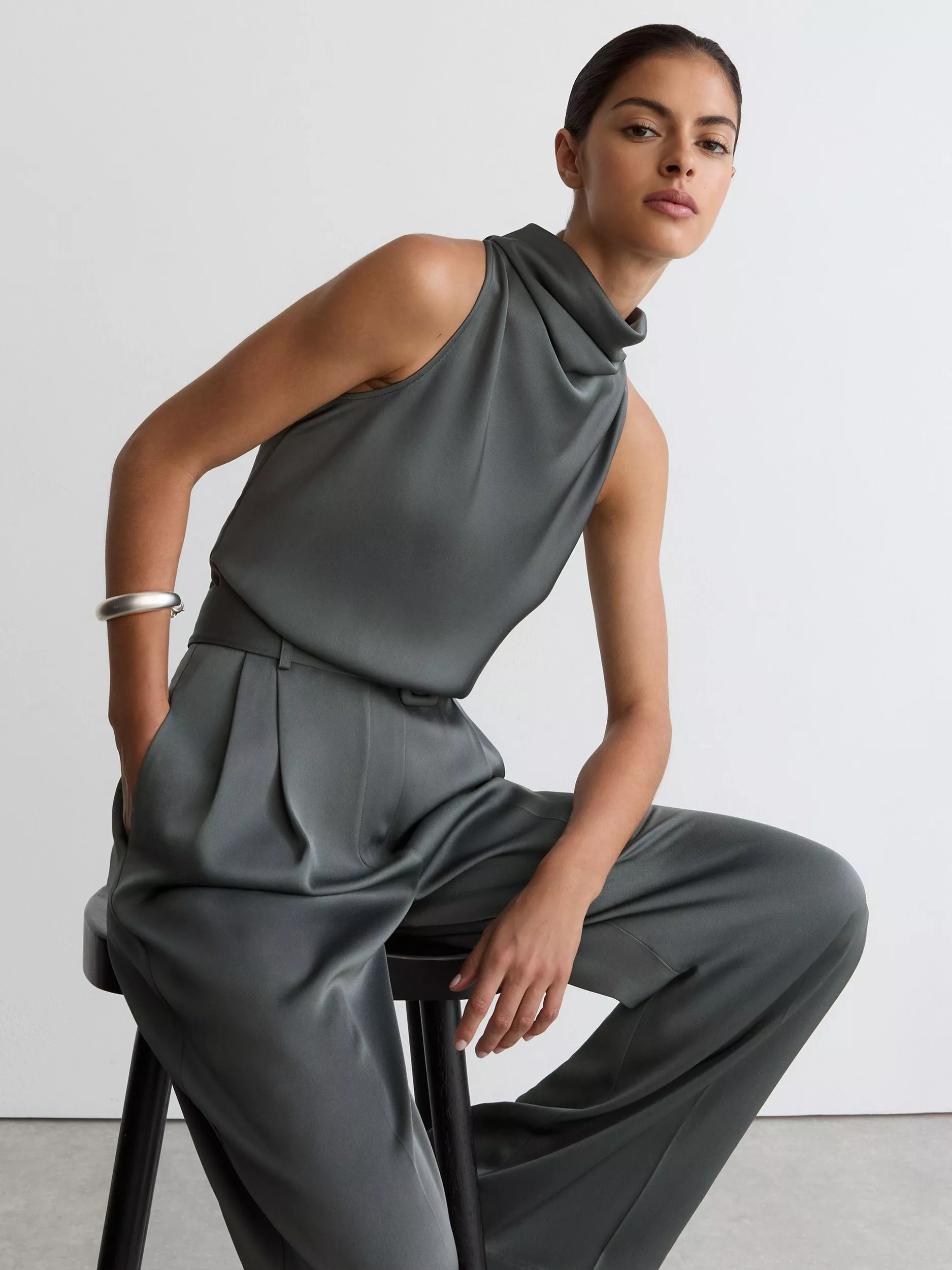 Fashion model in charcoal sleeveless high-neck top and wide-leg trousers, studio portrait on stool