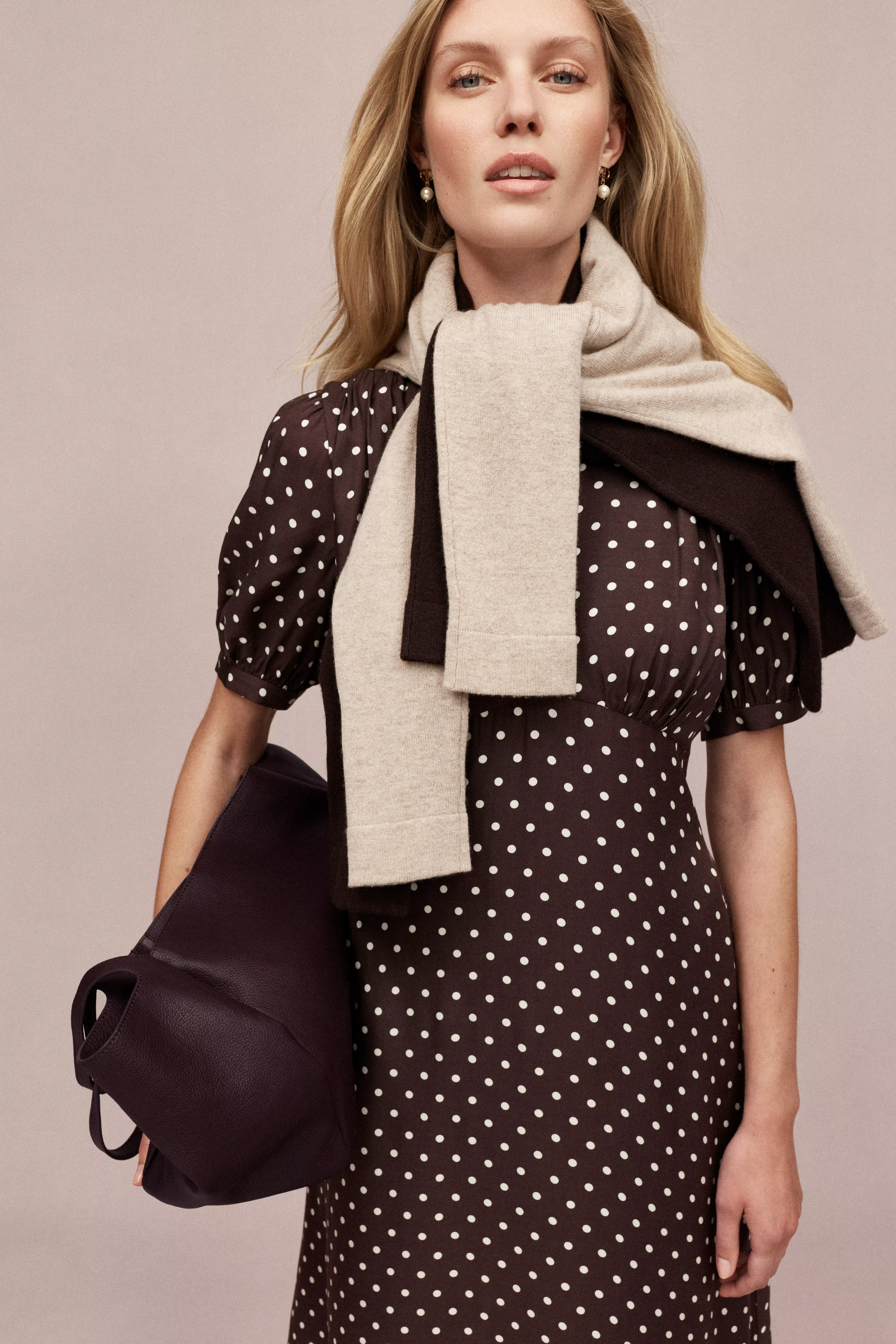 Blonde model in brown polka dot midi dress with beige scarf, pearl earrings and leather bag, studio fashion shot