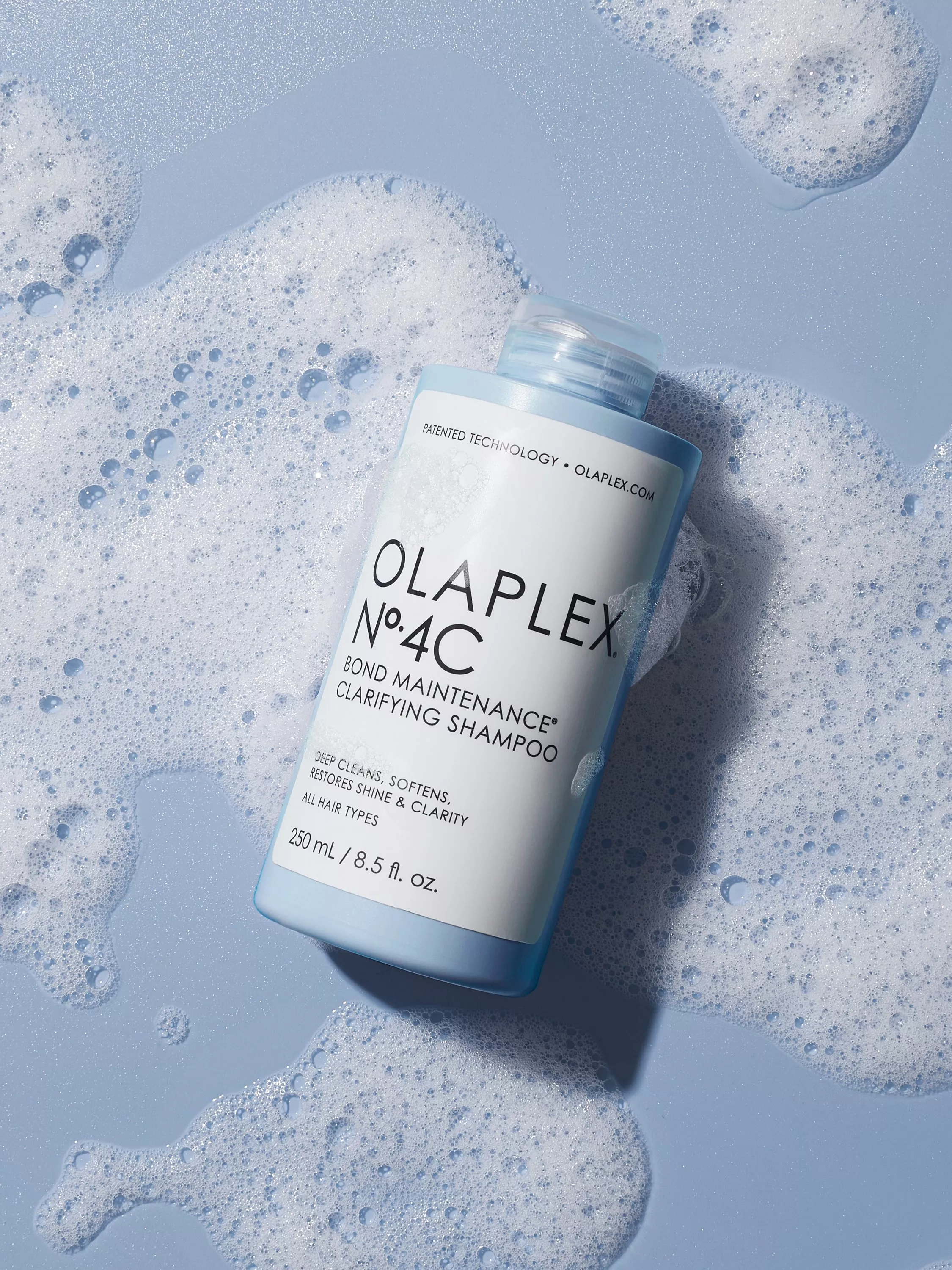 Olaplex No. 4C Clarifying Shampoo bottle on a blue surface with white soap suds around it.