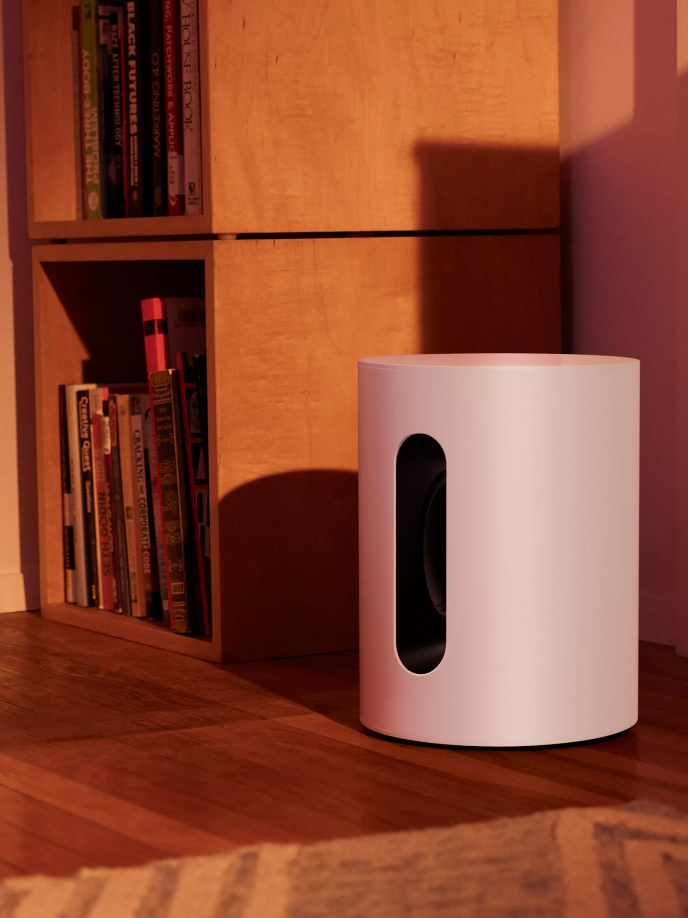 Modern white cylindrical home air purifier beside wooden bookshelf in warm evening light, minimalist living room decor