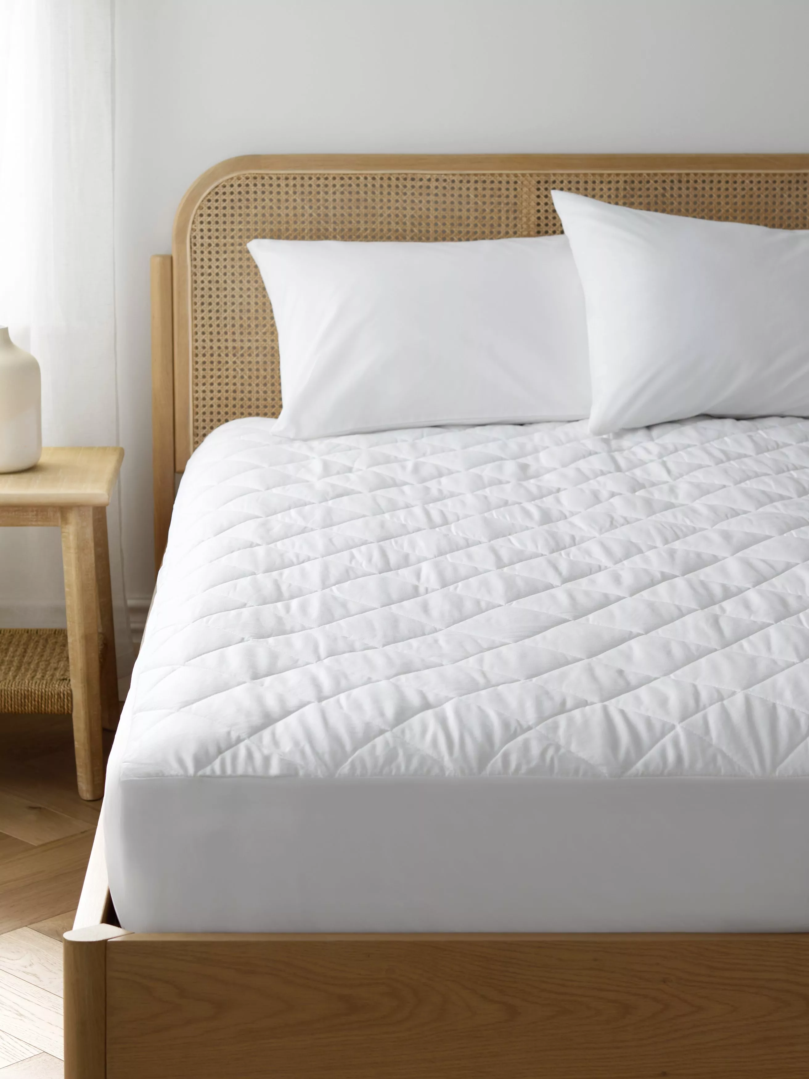 Minimalist bedroom with white quilted mattress topper on bed, cane headboard and wooden bedside table