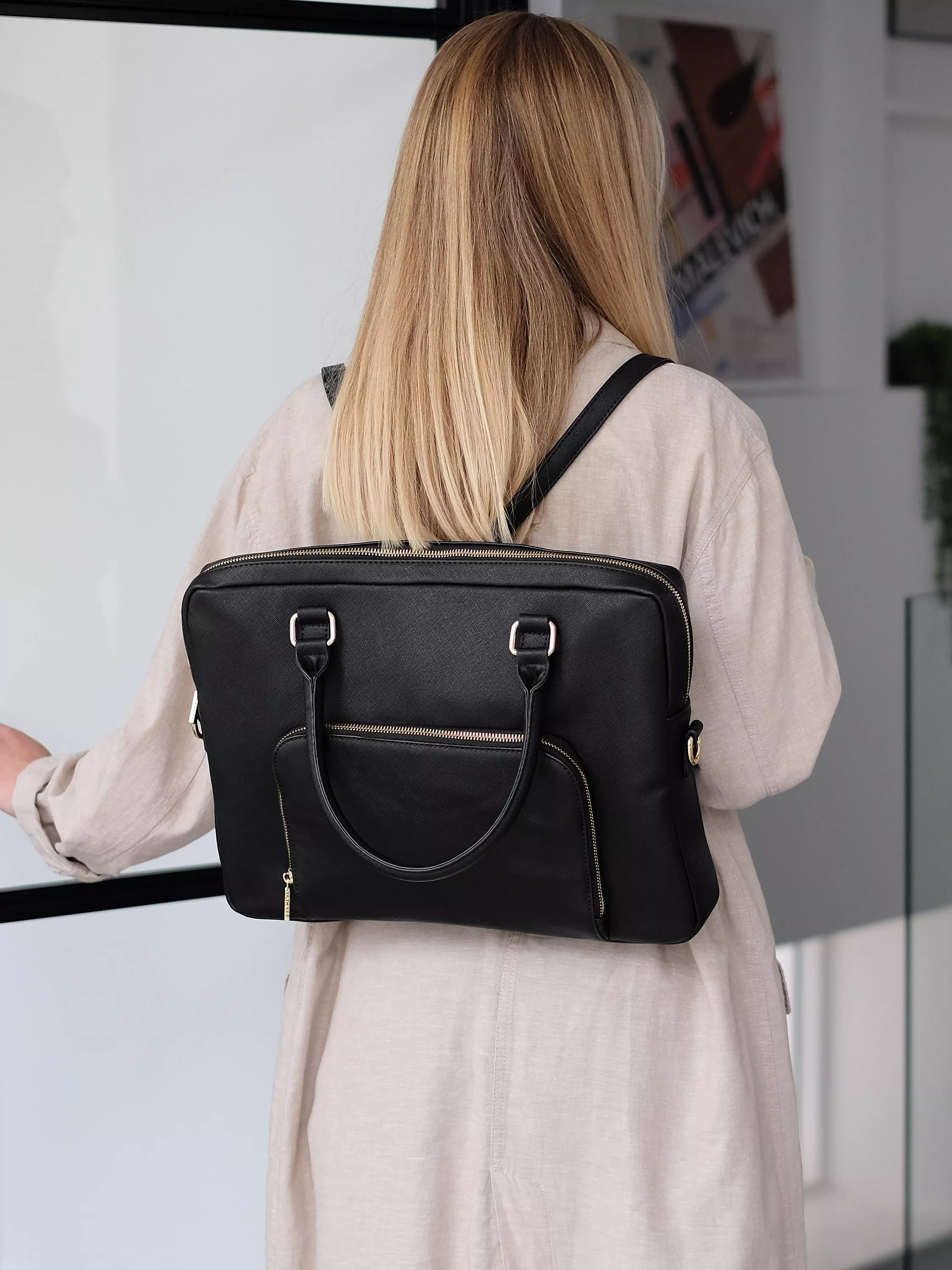 Woman wearing a black leather laptop backpack with gold zip details, ideal for office commuting and work travel
