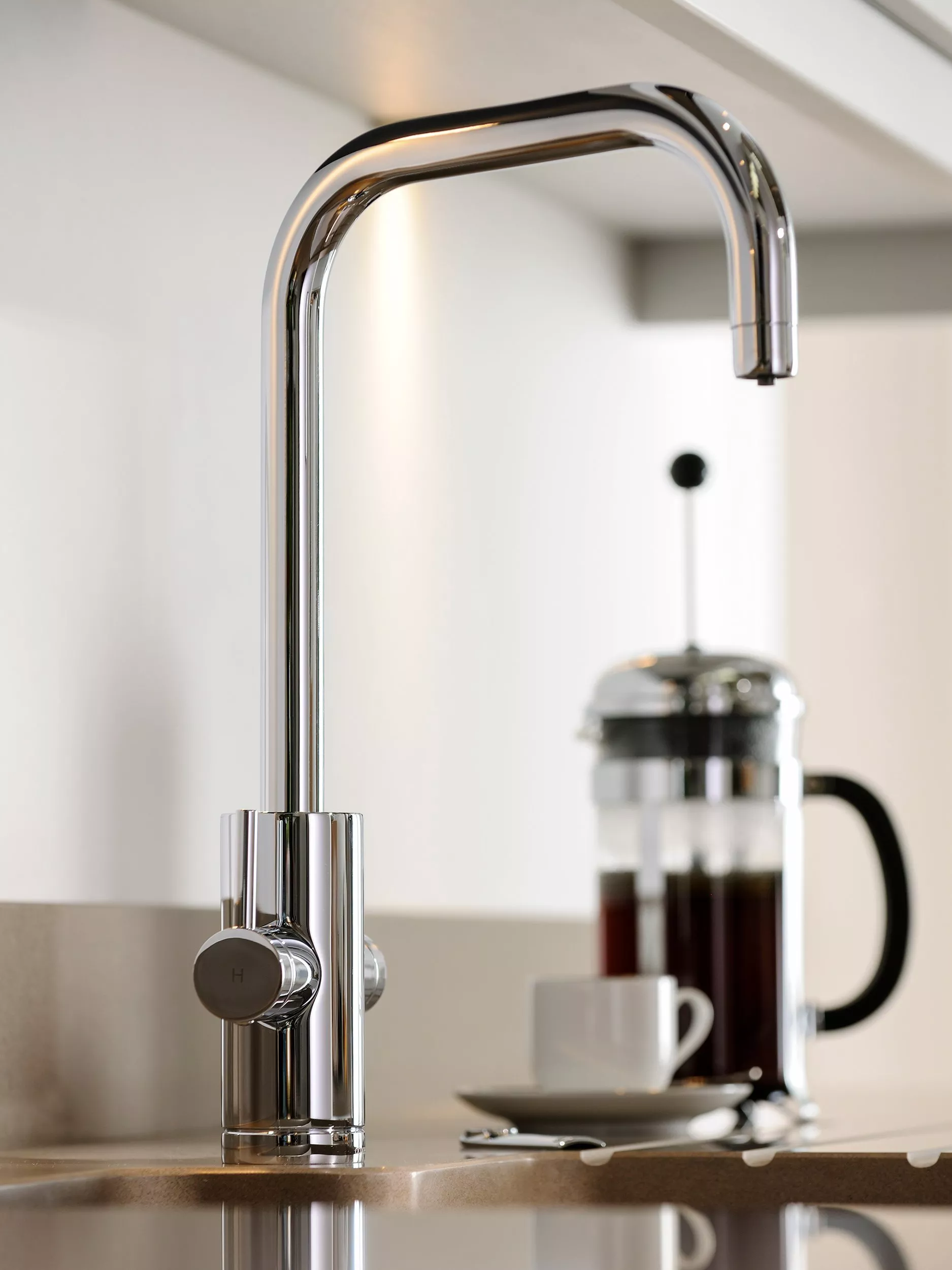 Chrome kitchen tap with single lever control above sink, modern minimalist worktop and coffee press in background
