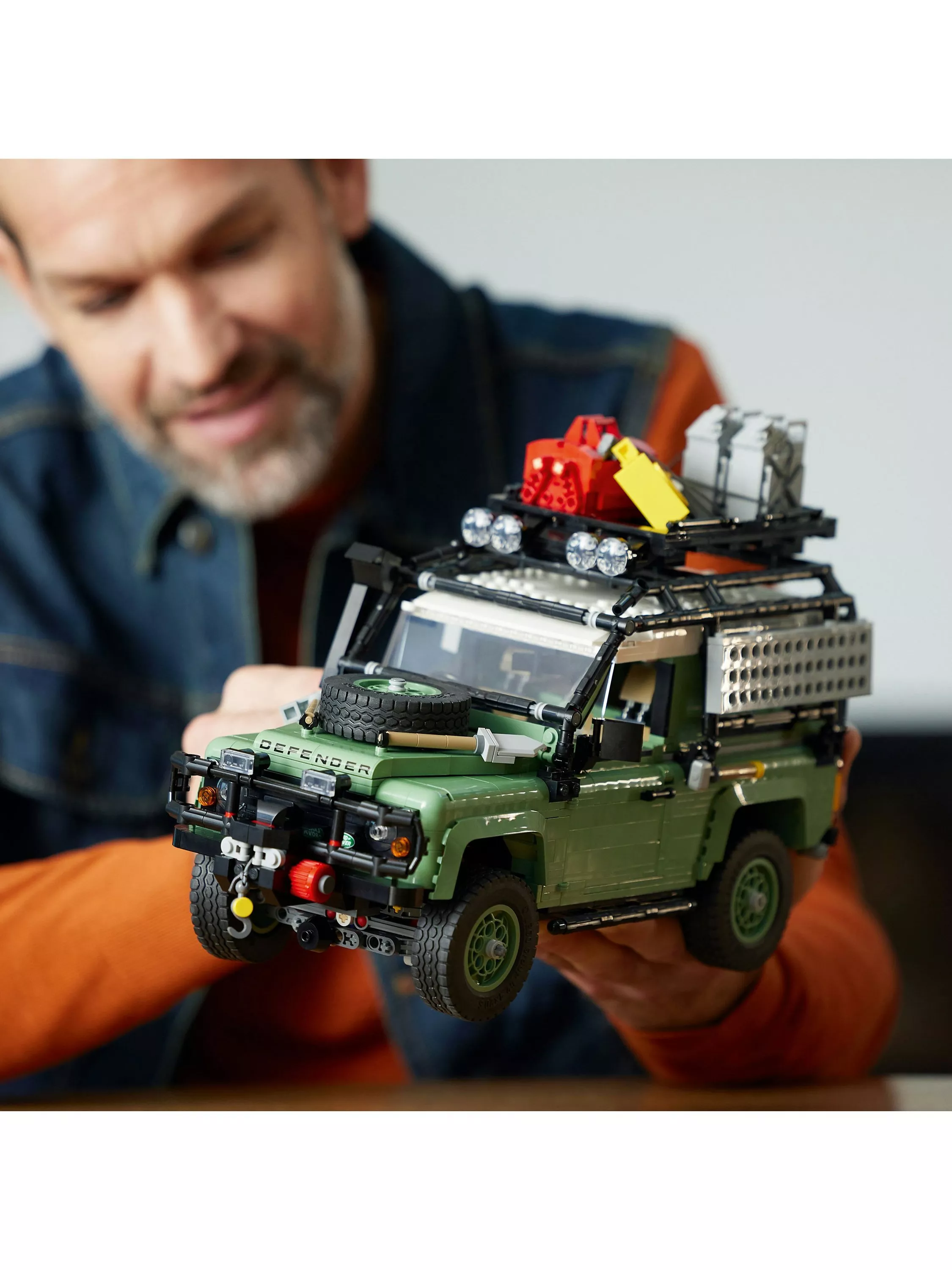 Man holding LEGO Technic Land Rover Defender model with roof rack, spare wheel and accessories, close-up view