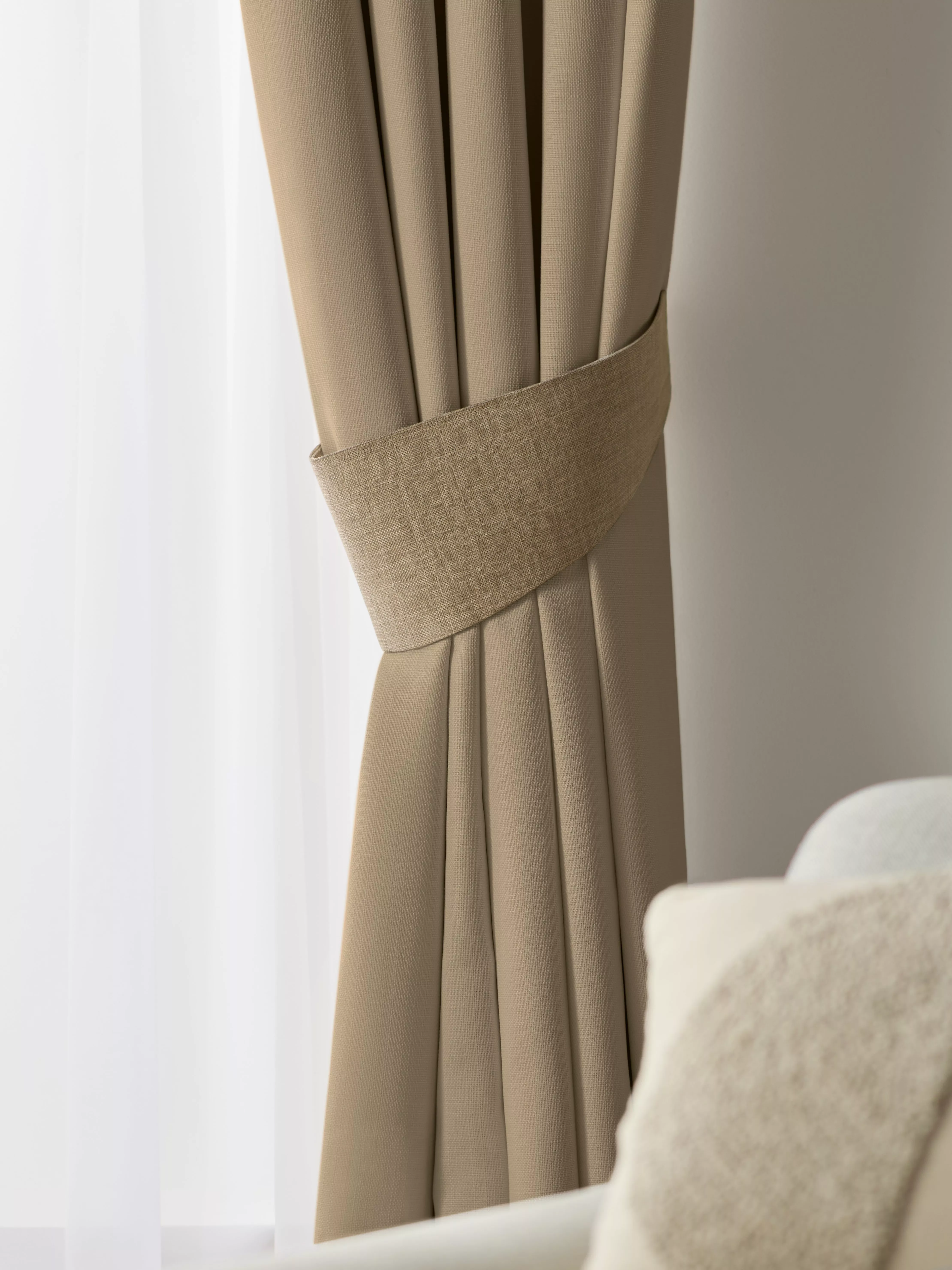 Beige blackout curtain with matching tieback, styled beside sheer window voile in modern neutral living room.