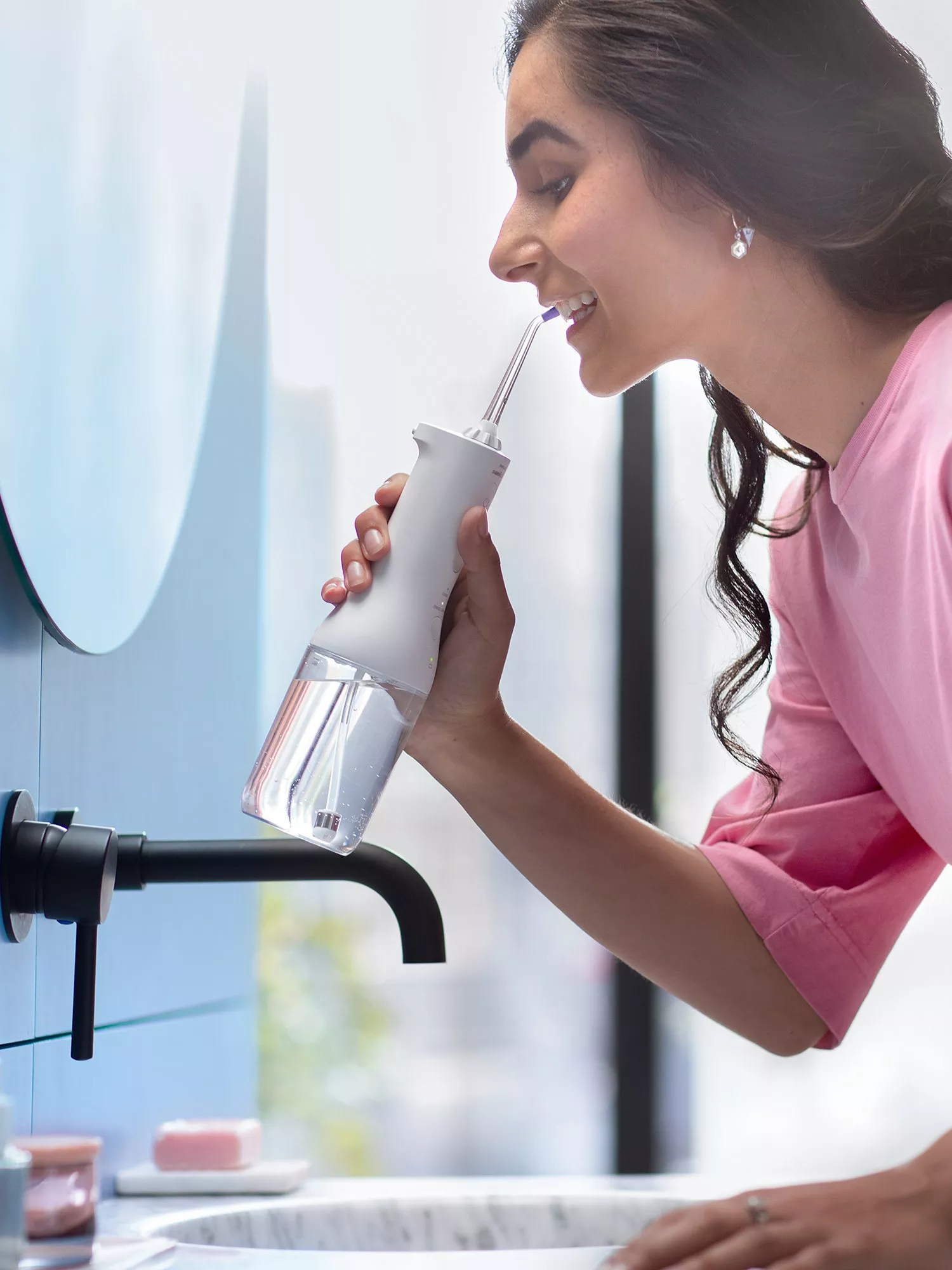 Woman using a cordless water flosser at bathroom sink, close-up dental hygiene routine with modern mirror and tap