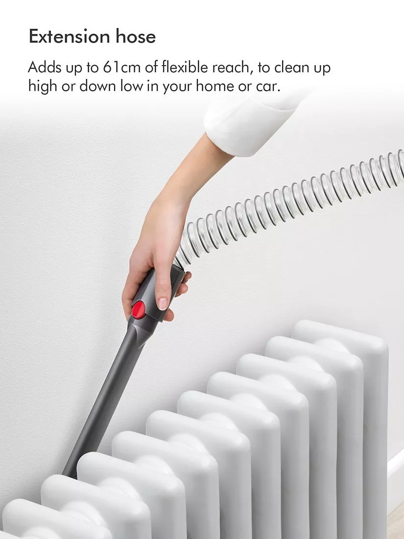 Woman using cordless stick vacuum cleaner on kitchen floor in modern grey kitchen with pendant lighting