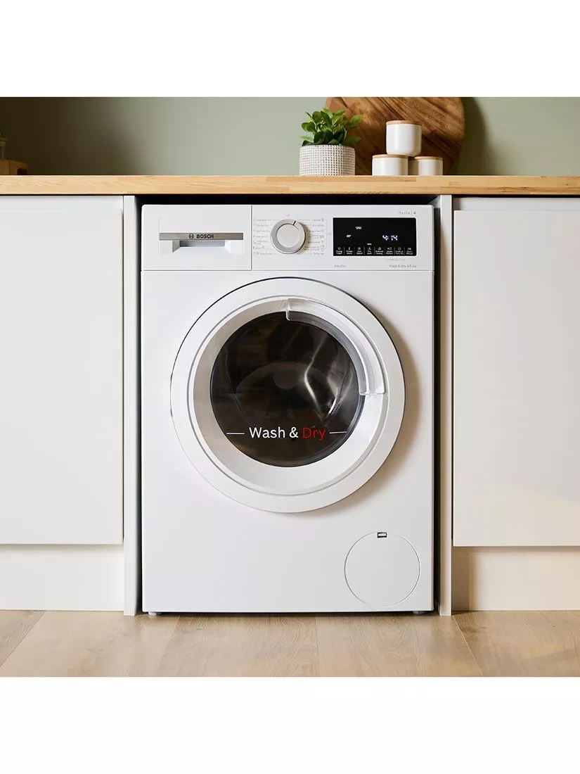 Integrated Bosch washer dryer in modern kitchen cabinet with wood worktop, display panel and potted plant above