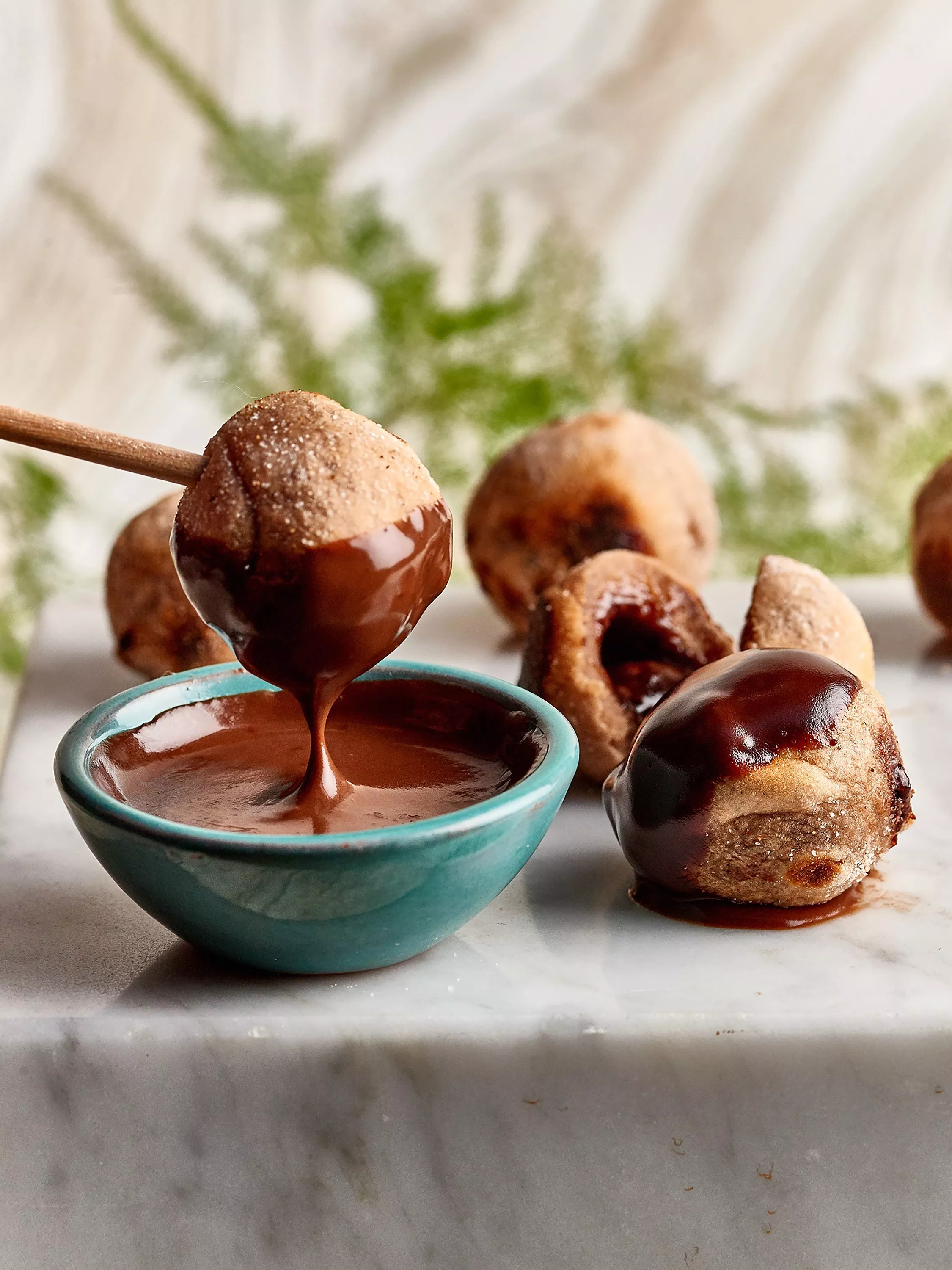 Chocolate doughnut holes dipped in rich chocolate sauce in a turquoise bowl on a marble board, close-up view