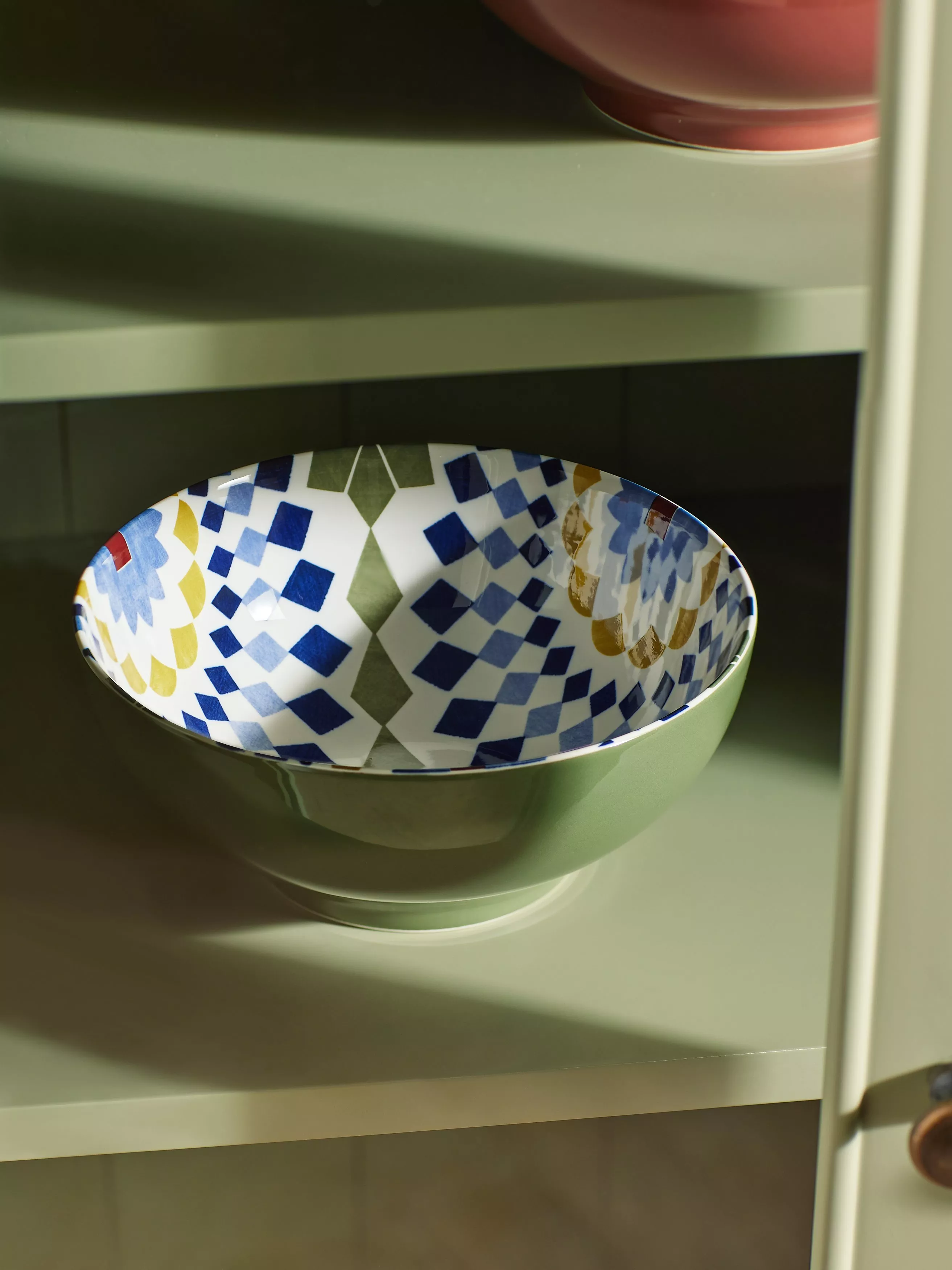 Colourful patterned ceramic bowl on a kitchen shelf, featuring blue geometric tiles and floral design in sunlight