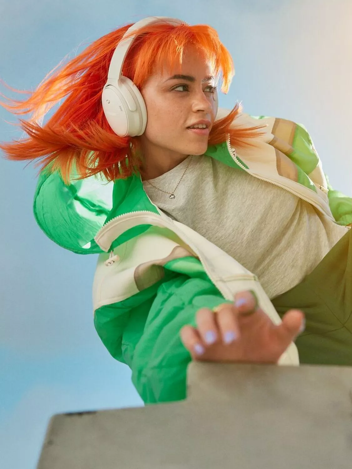 Young woman with orange hair wearing white wireless headphones, dancing in green jacket, music lifestyle portrait