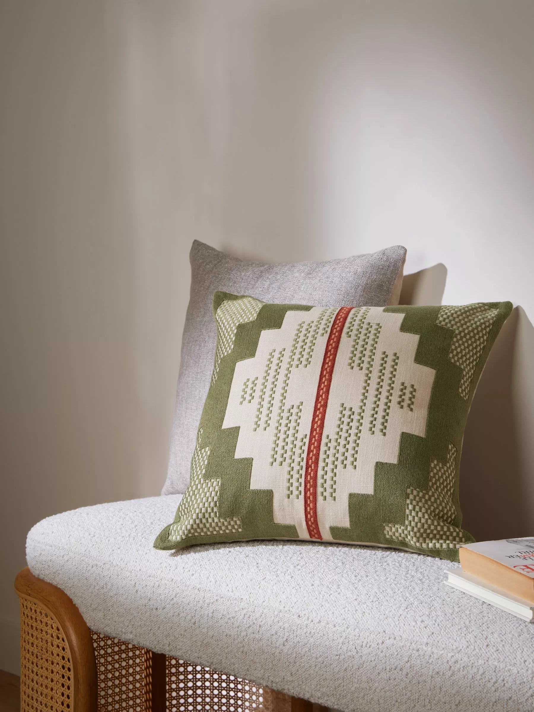 Green geometric woven cushion on a boucle bench with cane frame, styled with grey pillow and book stack