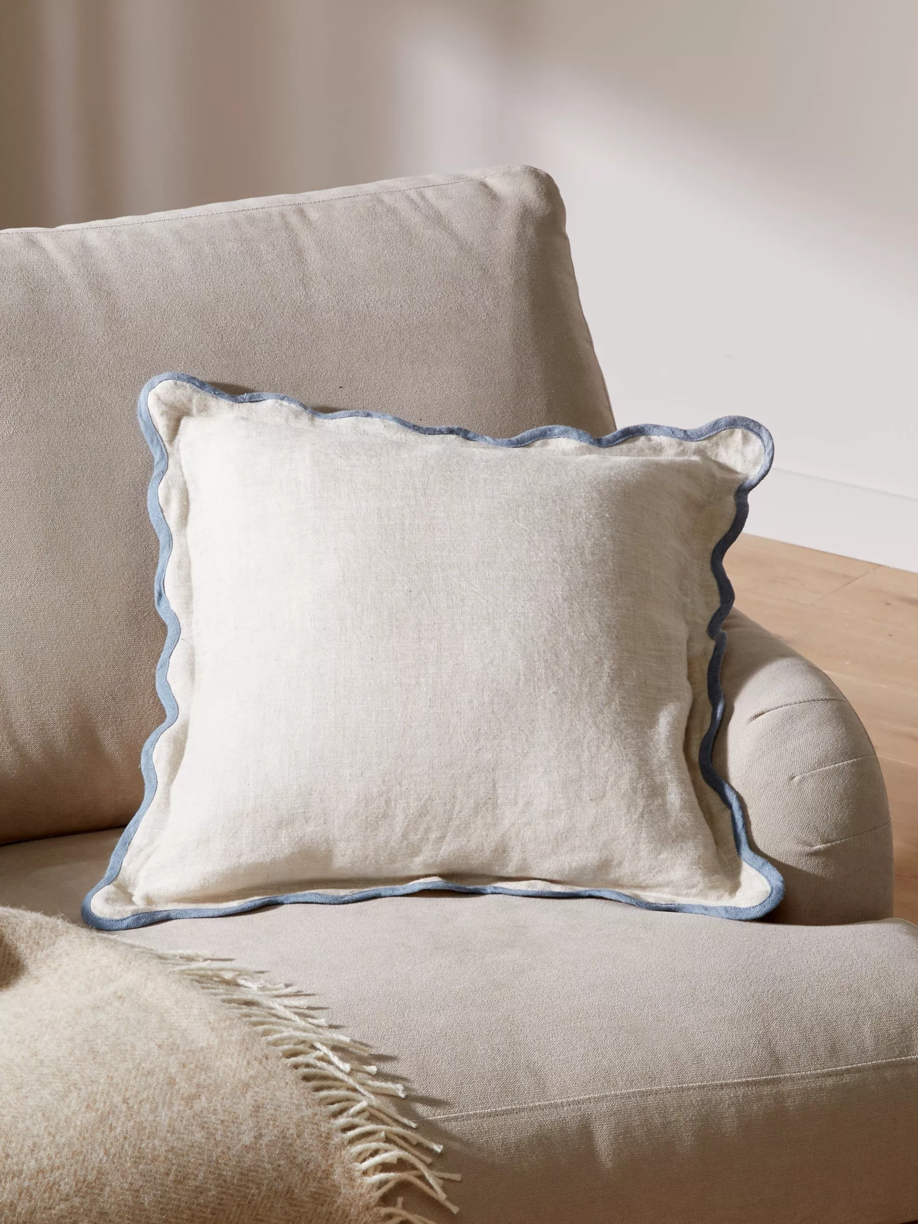 Beige linen cushion with a blue scalloped edge on a beige sofa
