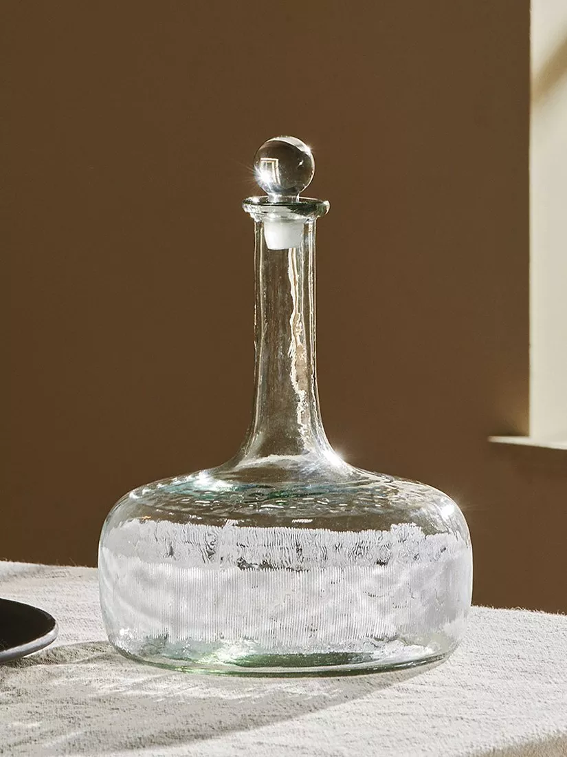 Glass whisky decanter and two tumblers with amber spirit on marble countertop in natural sunlight shadows