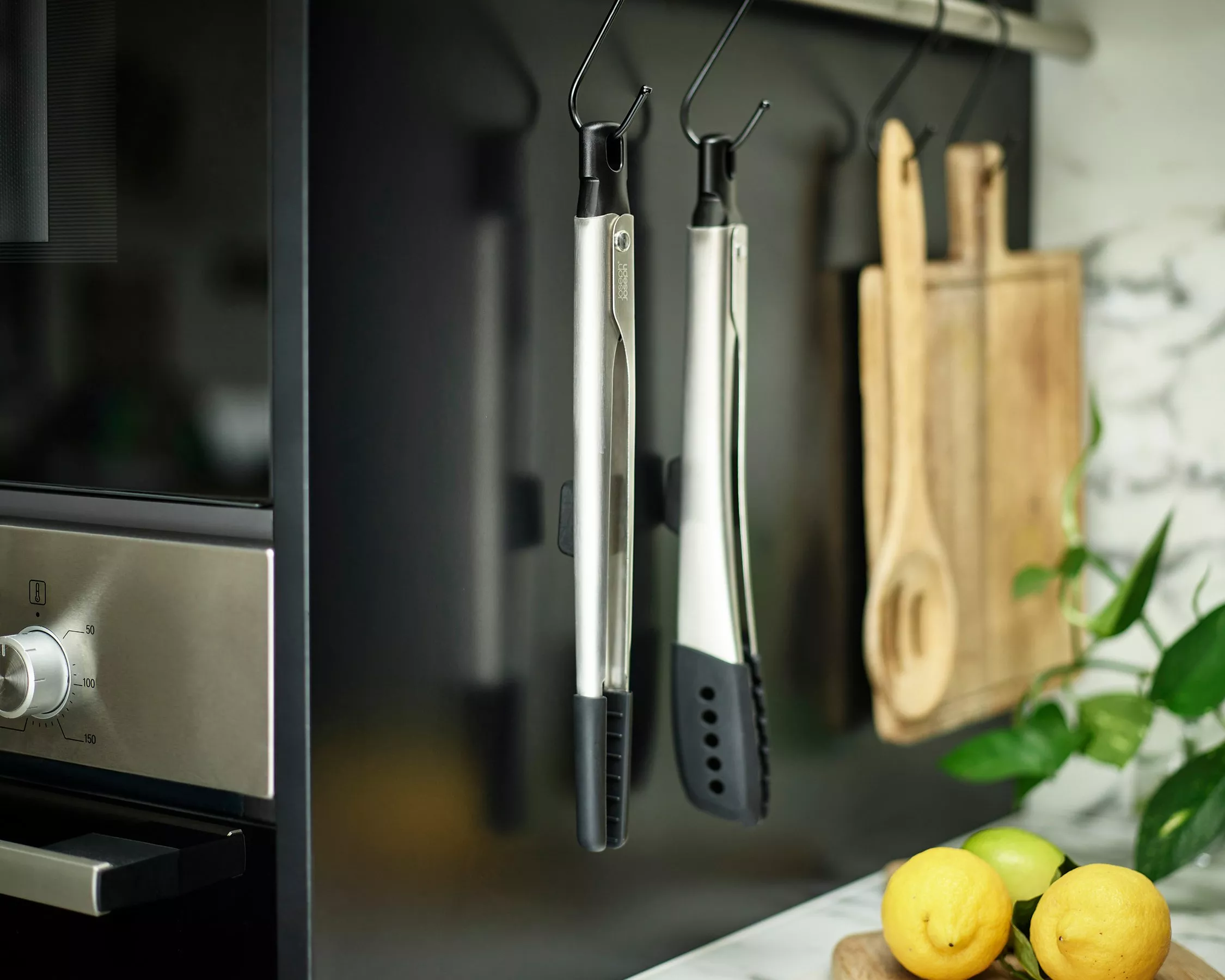 Stainless steel kitchen tongs hanging on a rail beside wooden boards, lemon and lime on worktop in modern kitchen