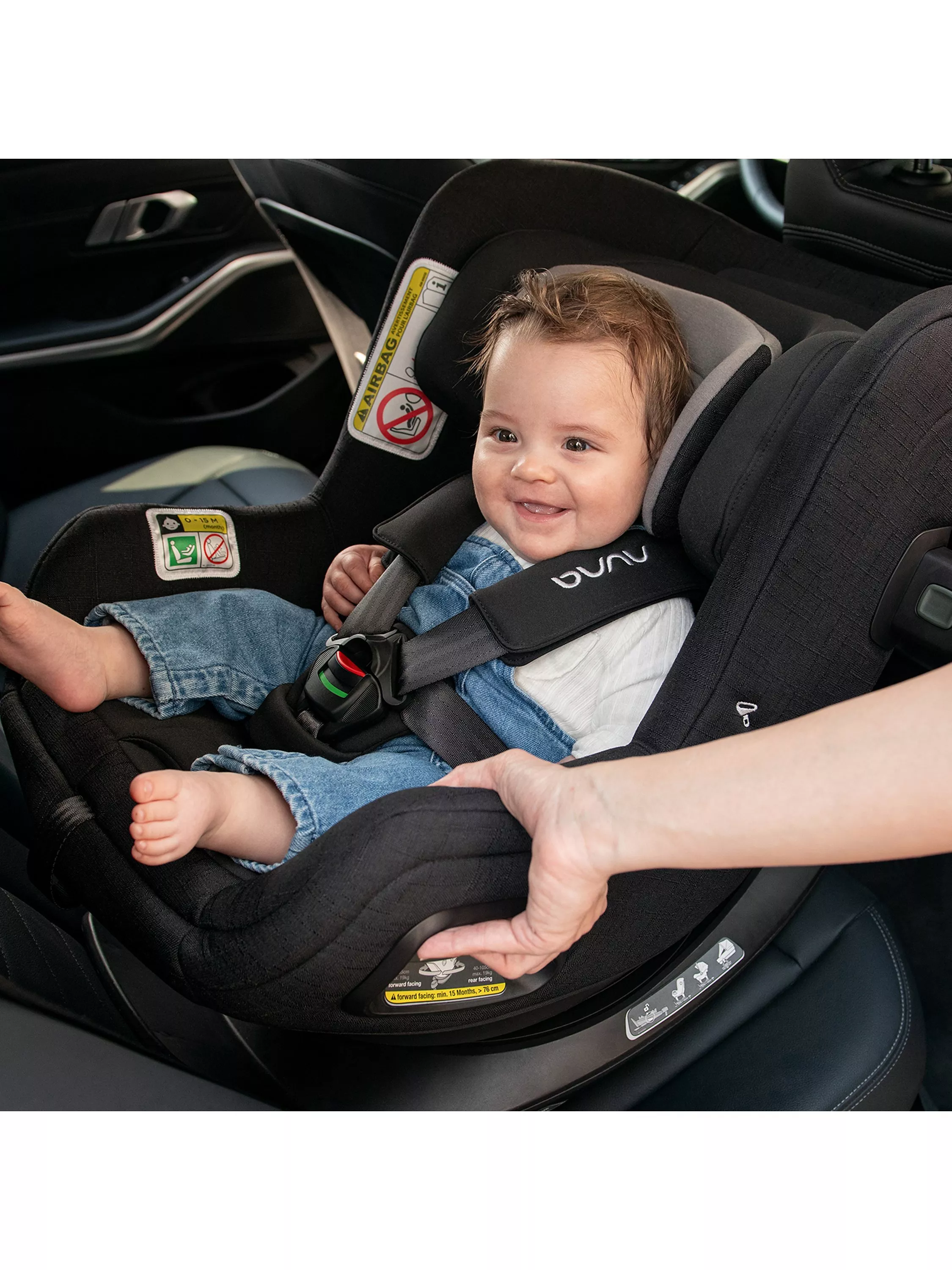 Smiling baby secured in a rear-facing infant car seat with five-point harness, showing safe travel setup in car interior