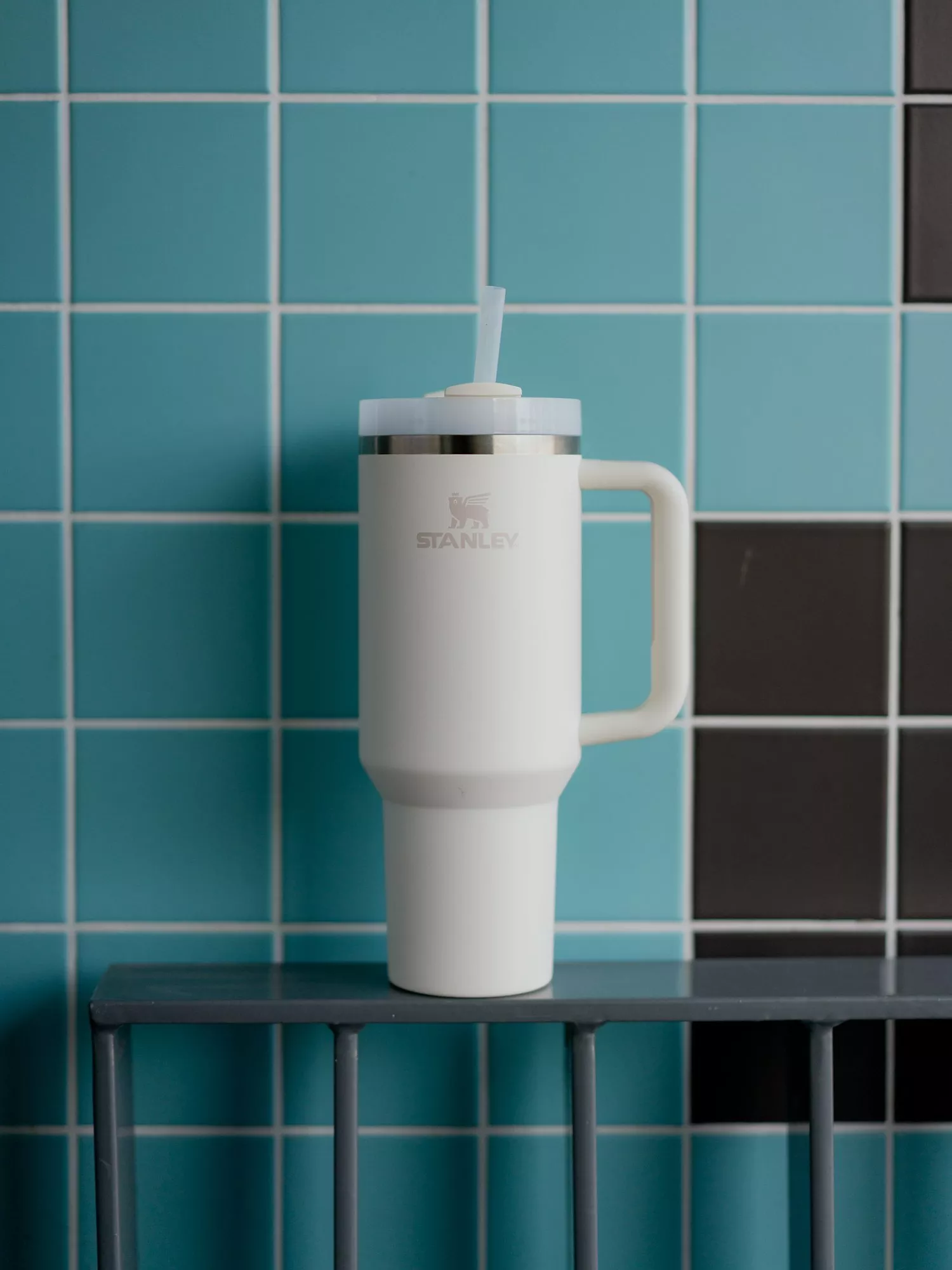 White Stanley insulated tumbler with handle and straw on shelf against blue and black tiled wall background