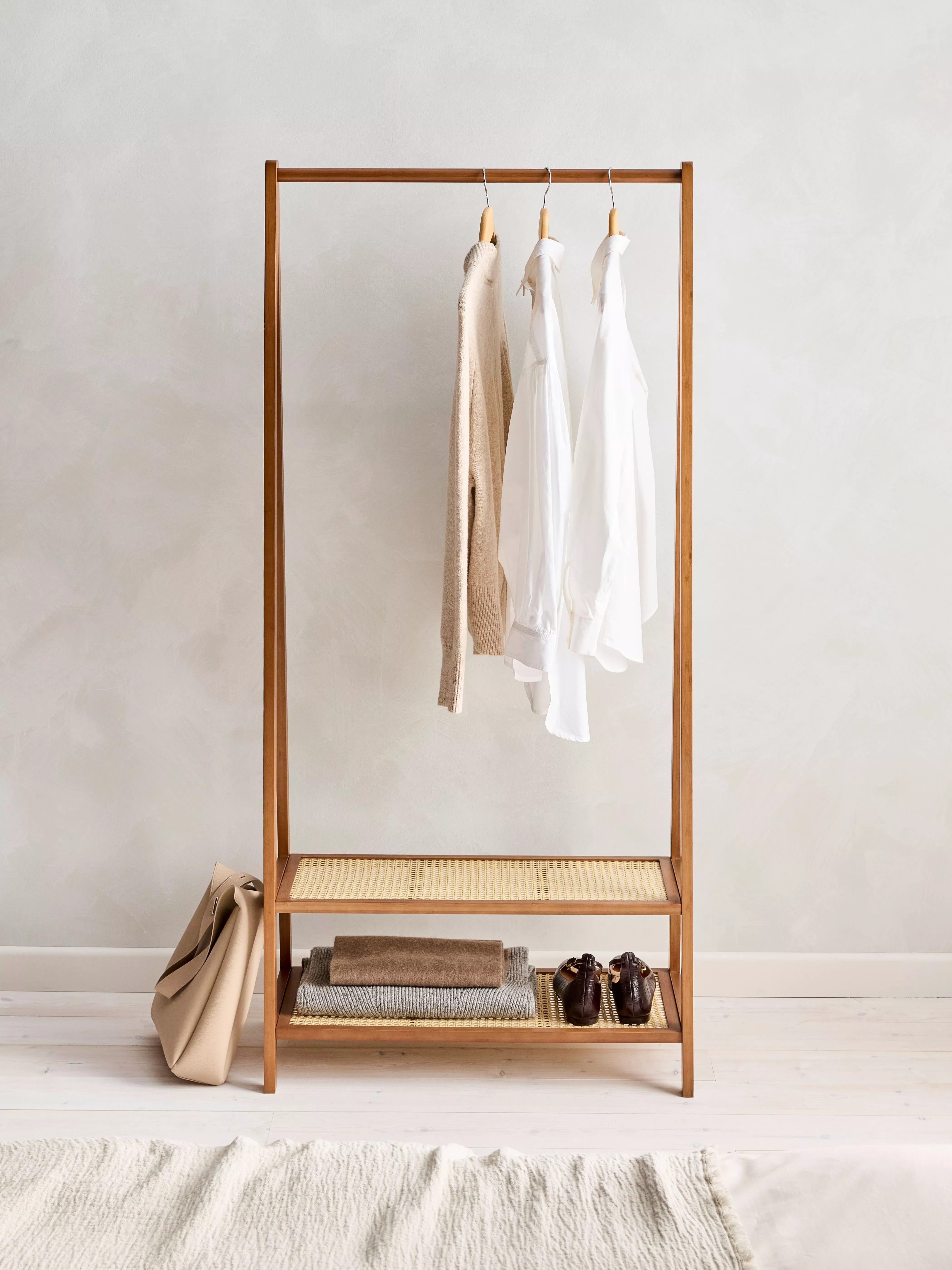 Minimalist wooden clothes rack with jackets, scarf and cap, plus green backpack on shelf in bright room