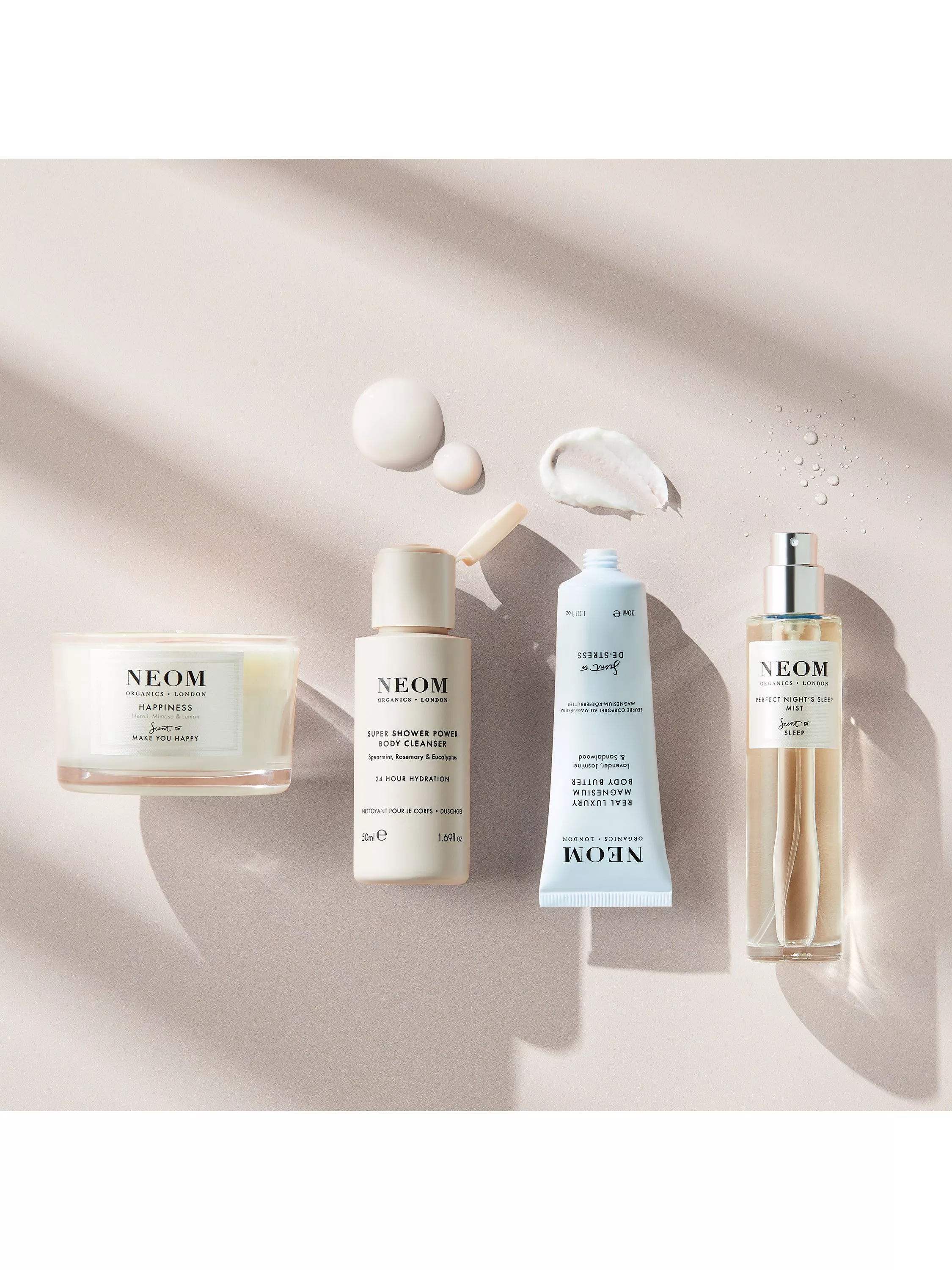 NEOM Organics London skincare set with candle, body cleanser, body butter and sleep mist on beige backdrop.