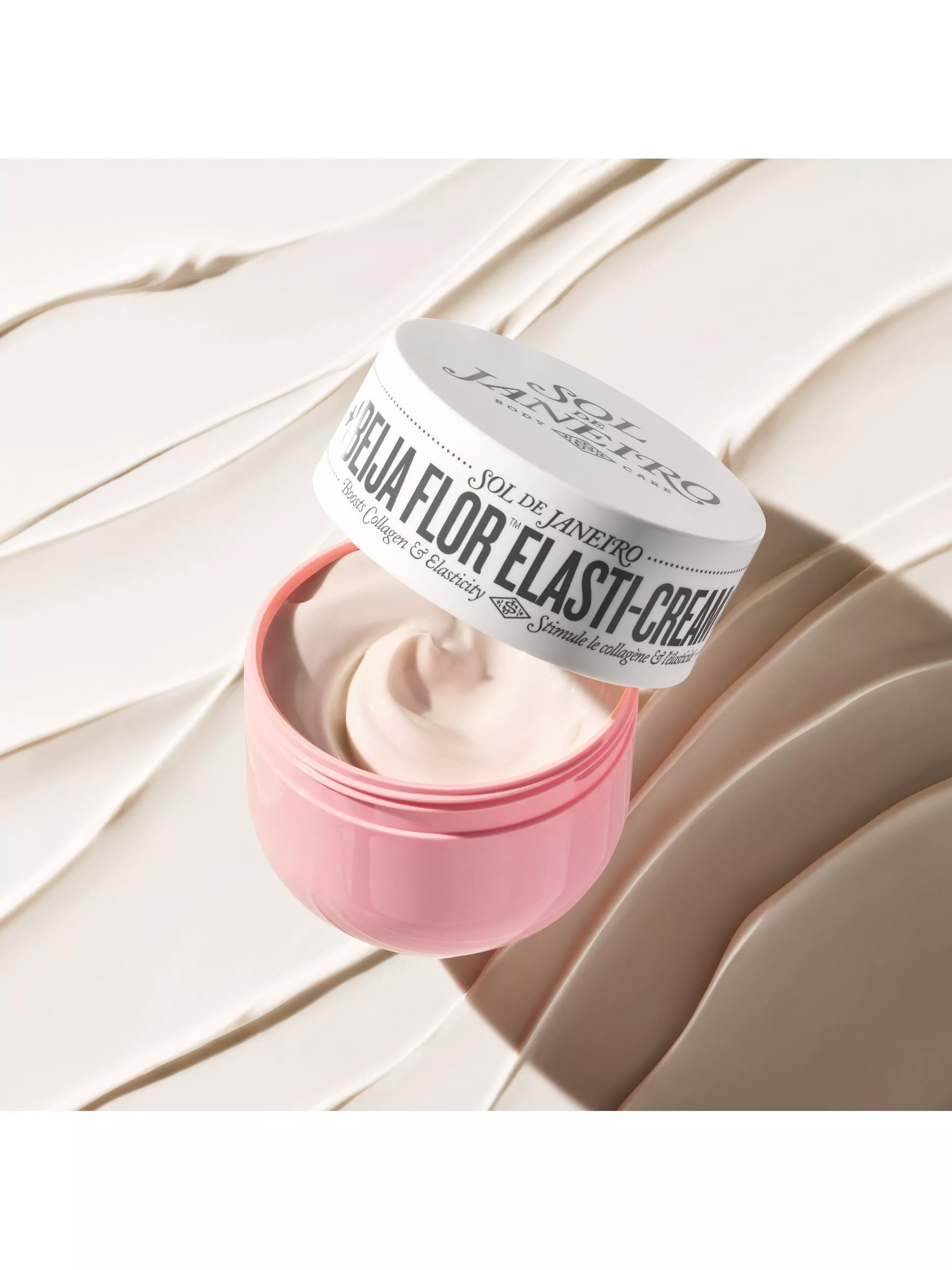 Sol de Janeiro Beija Flor Elasti-Cream jar open, showing pink moisturiser with lid on cream-textured backdrop