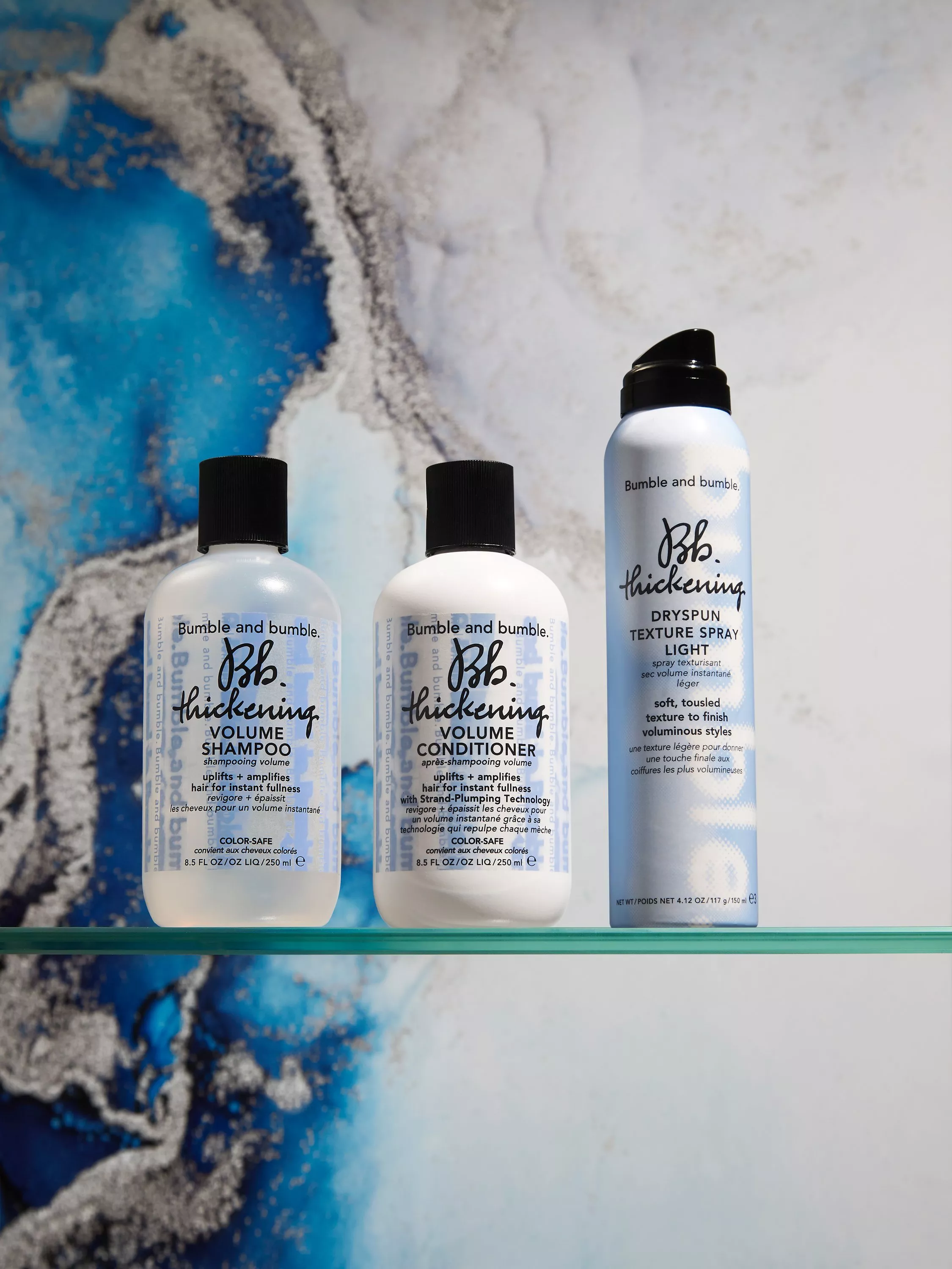 Bumble and bumble Thickening shampoo, conditioner and texture spray on glass shelf against blue marble wall