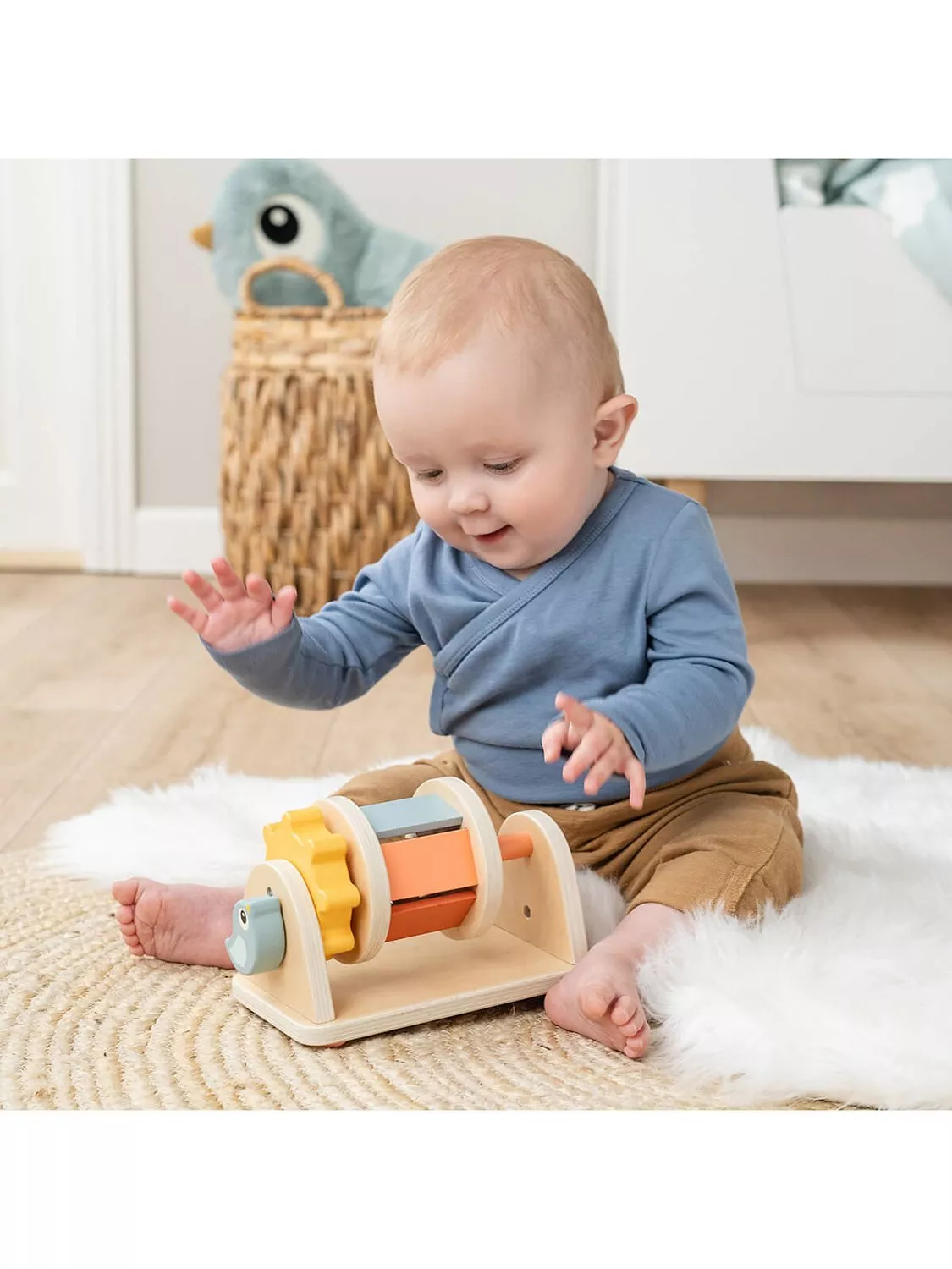Baby sitting on rug playing with wooden sensory toy in nursery, soft neutral décor and storage basket behind