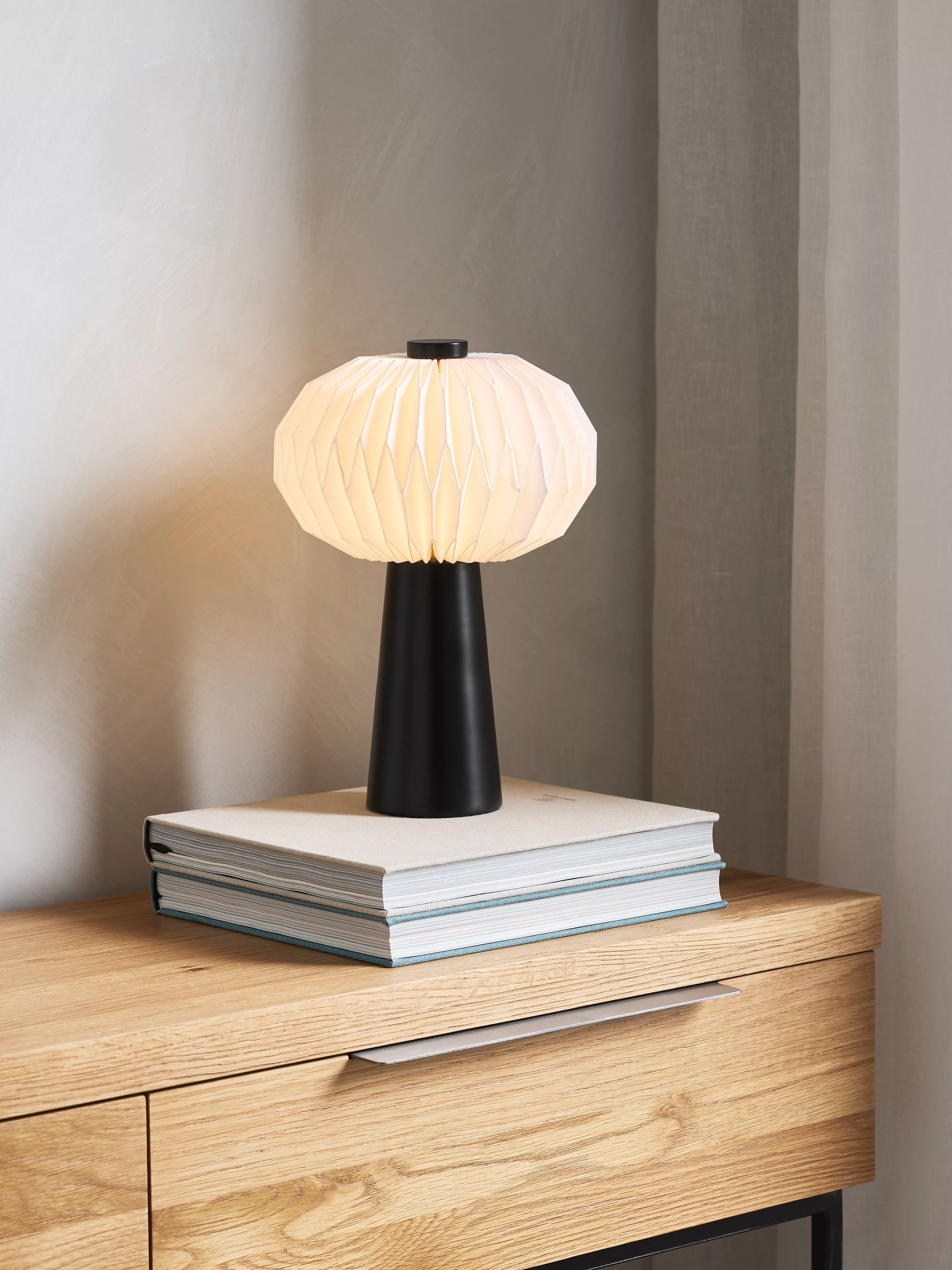 Black table lamp with a white shade on some books on a side board
