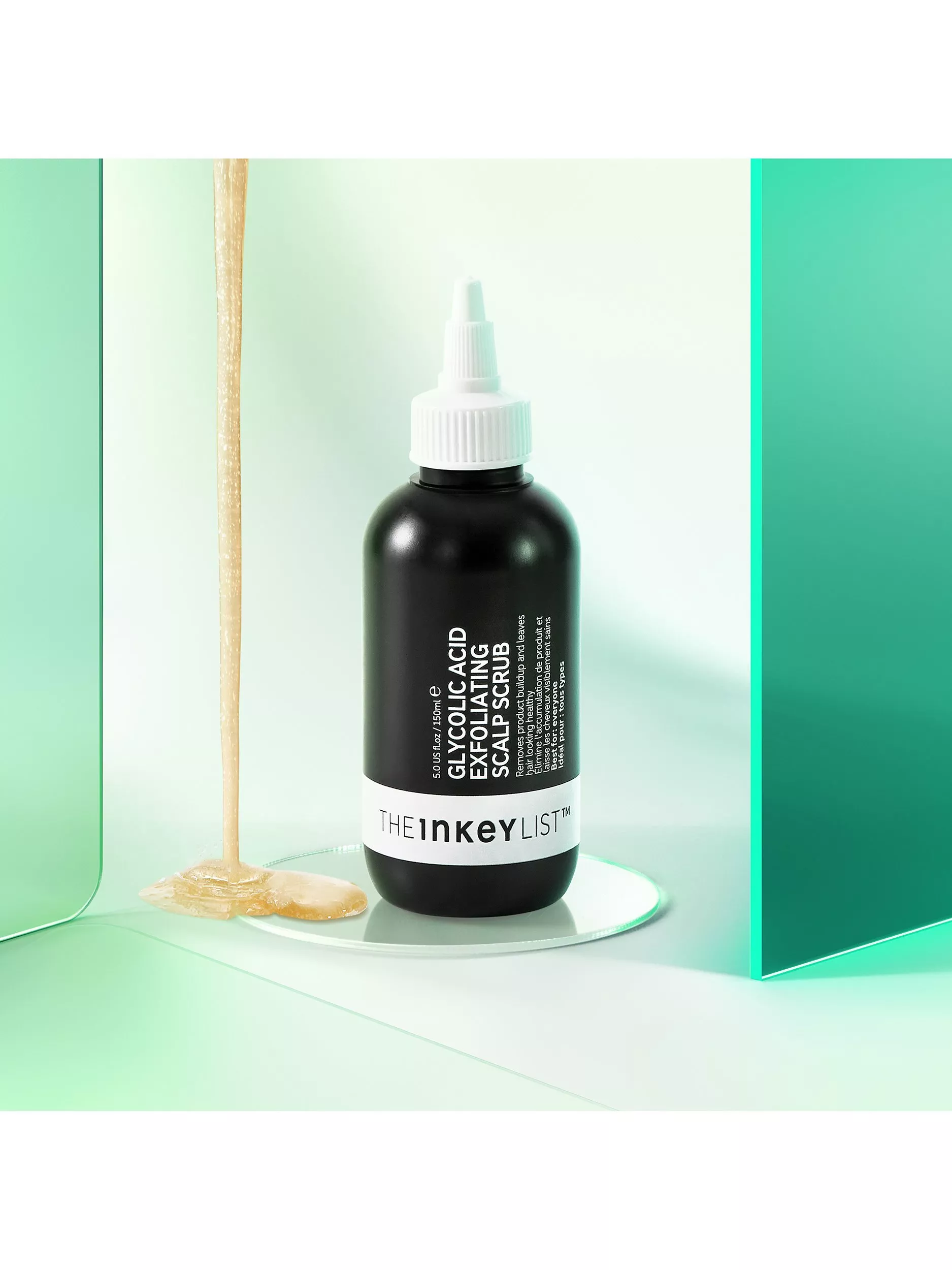 The INKEY List Glycolic Acid Exfoliating Scalp Scrub bottle on glass, with honey-like texture on mint backdrop