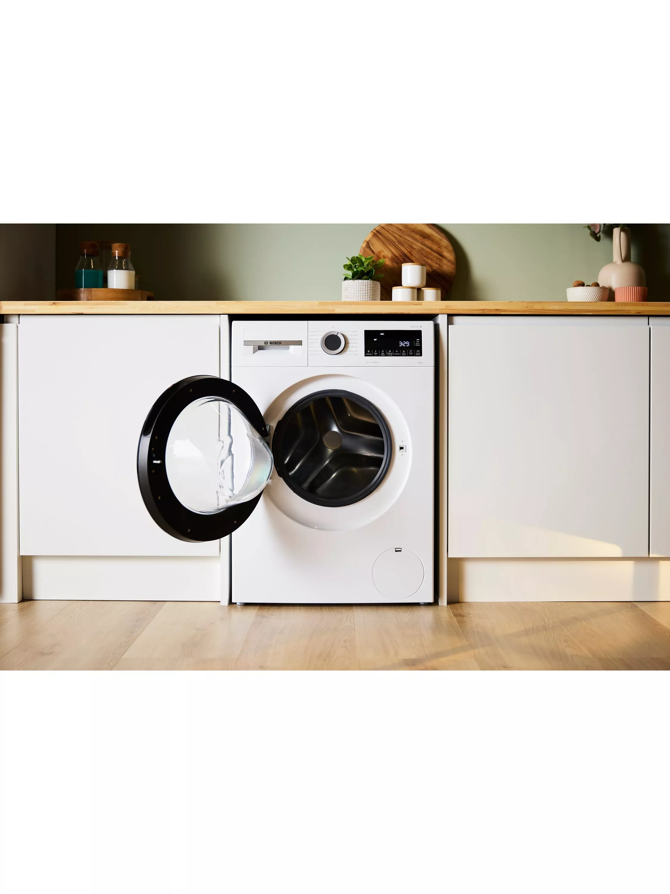 Modern laundry room with built-in white front-loading washing machine, open door, wooden worktop and décor