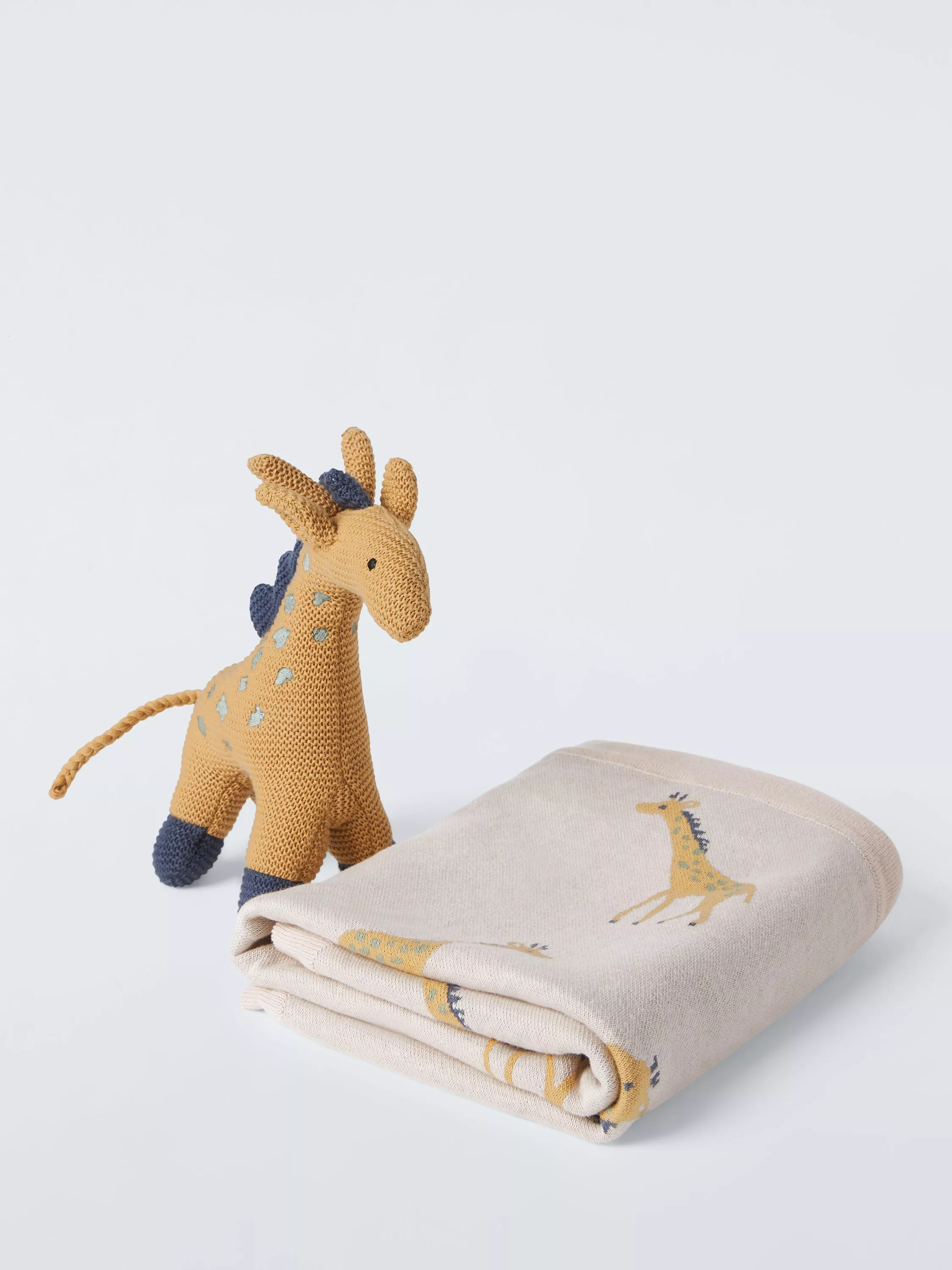 Knitted giraffe soft toy beside folded baby blanket with giraffe print, neutral nursery bedding gift set