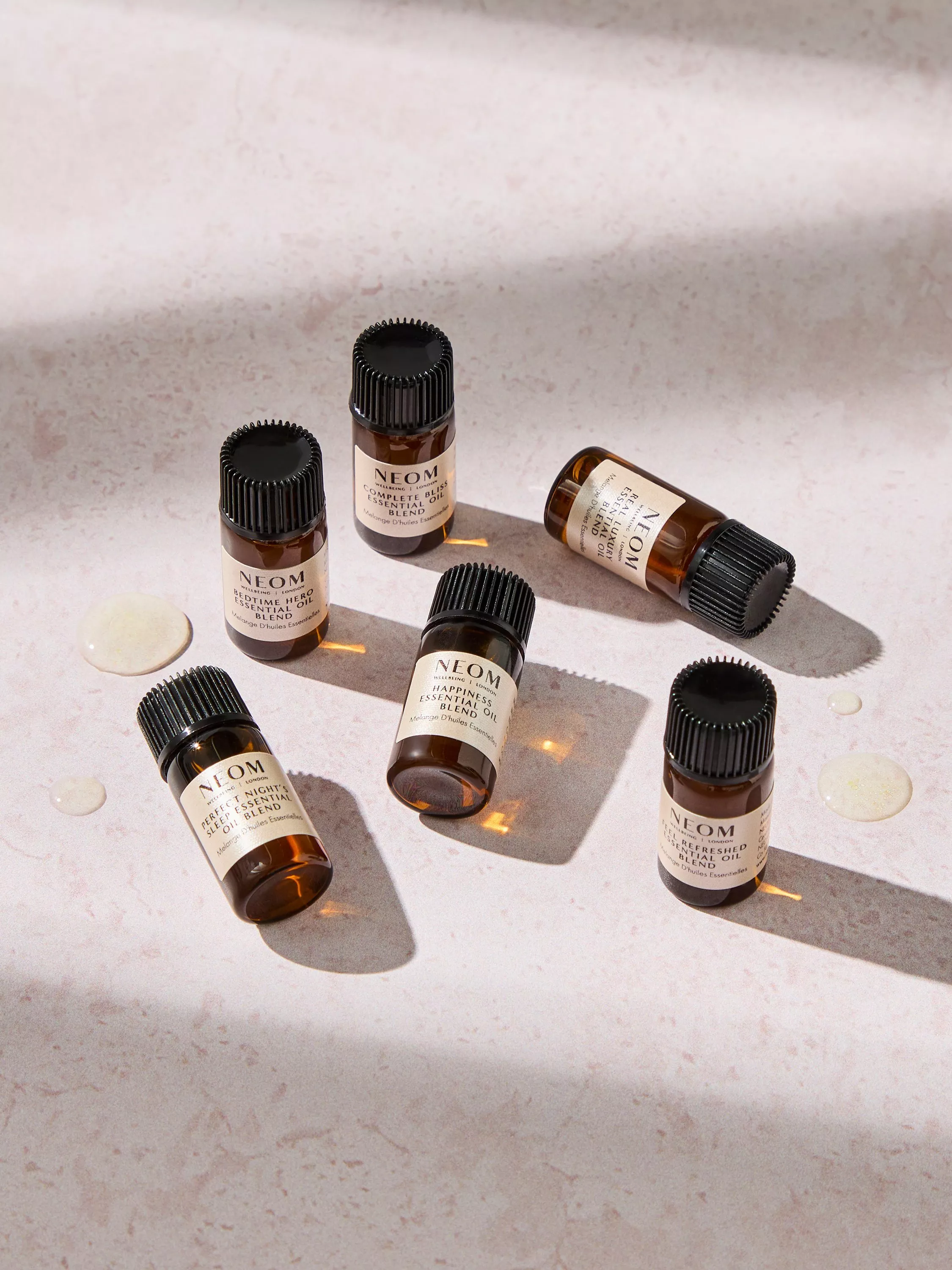 NEOM essential oil blend bottles on a marble surface with natural light and oil droplets, aromatherapy skincare flat lay