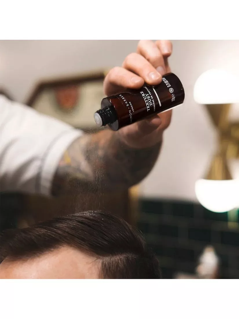 Barber applying hair styling powder to slick side-part hairstyle in barbershop for extra volume and texture