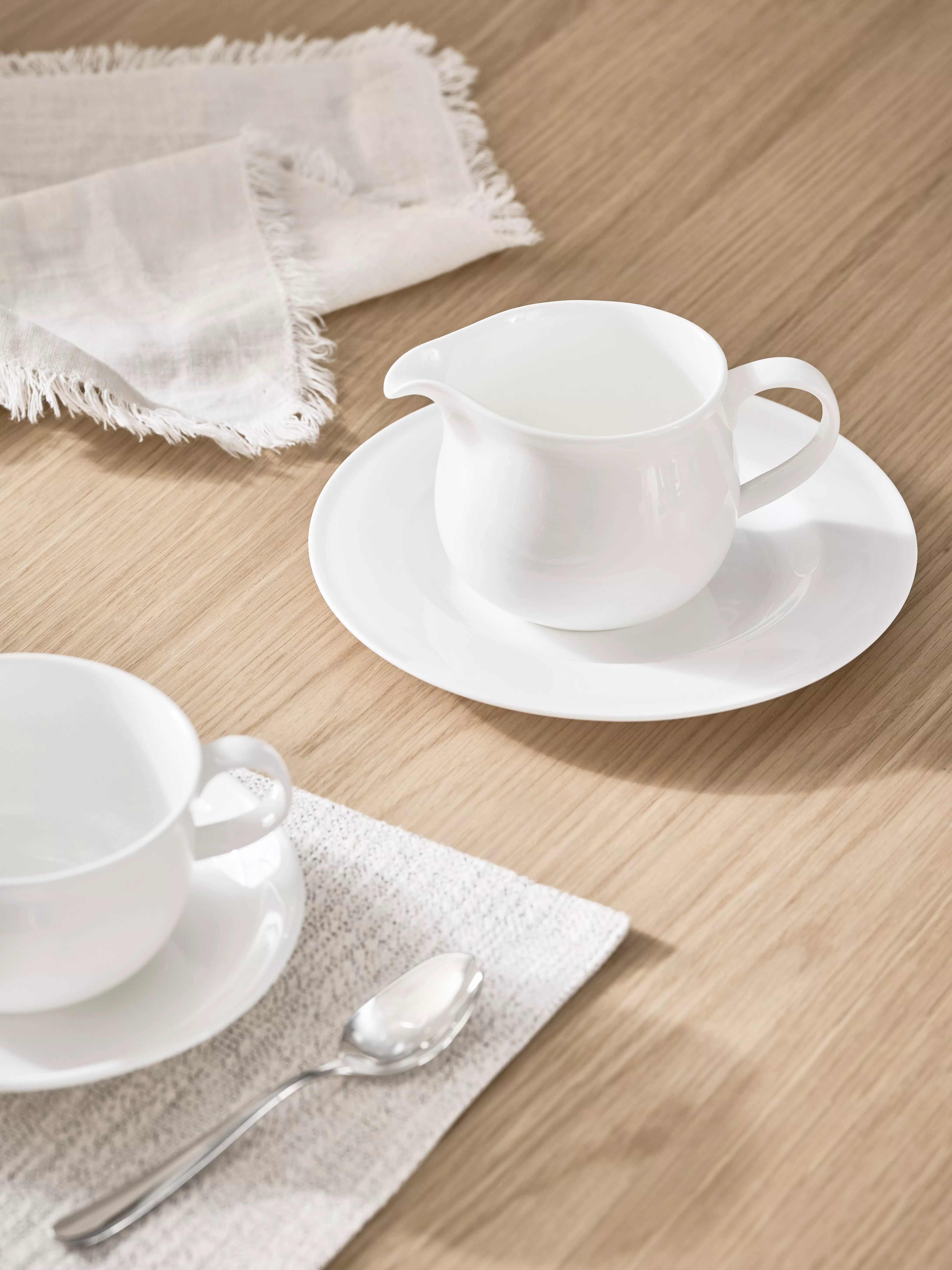 White porcelain tea set with blue floral pattern, cup and saucer, sugar bowl and jug on blue table runner