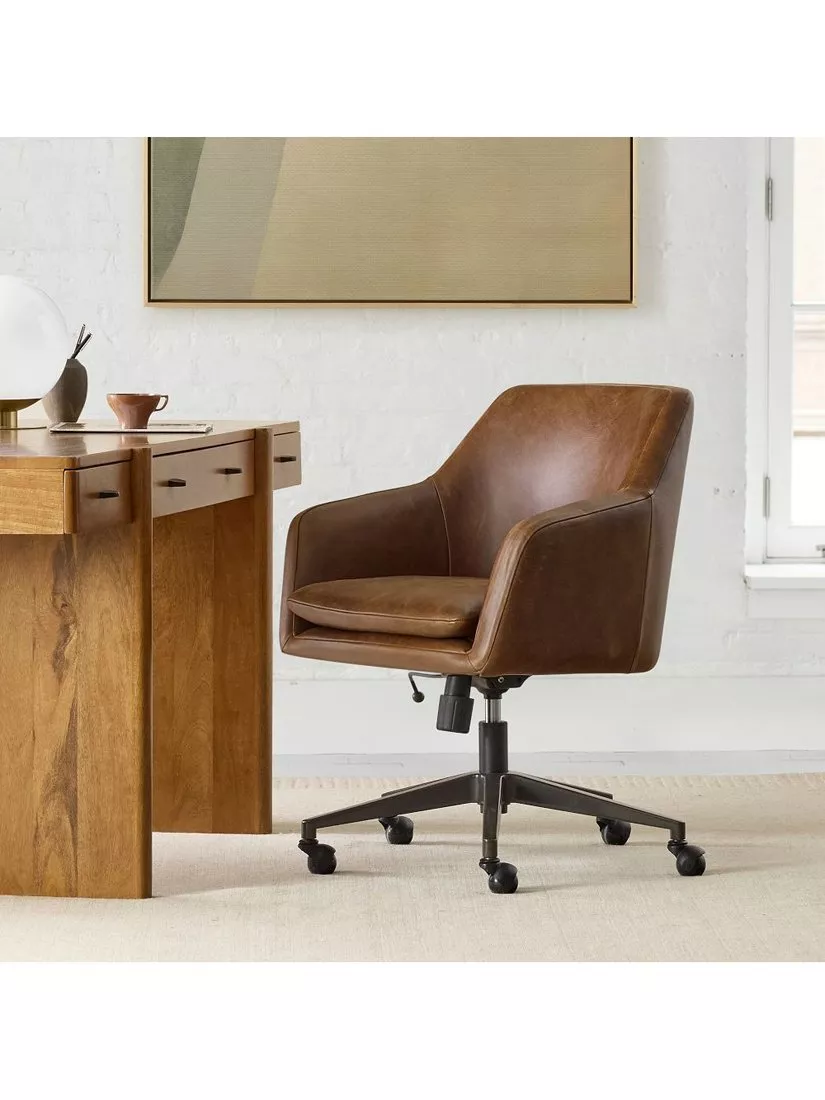 Brown leather swivel office chair on castors beside a wooden desk in a modern home office setting