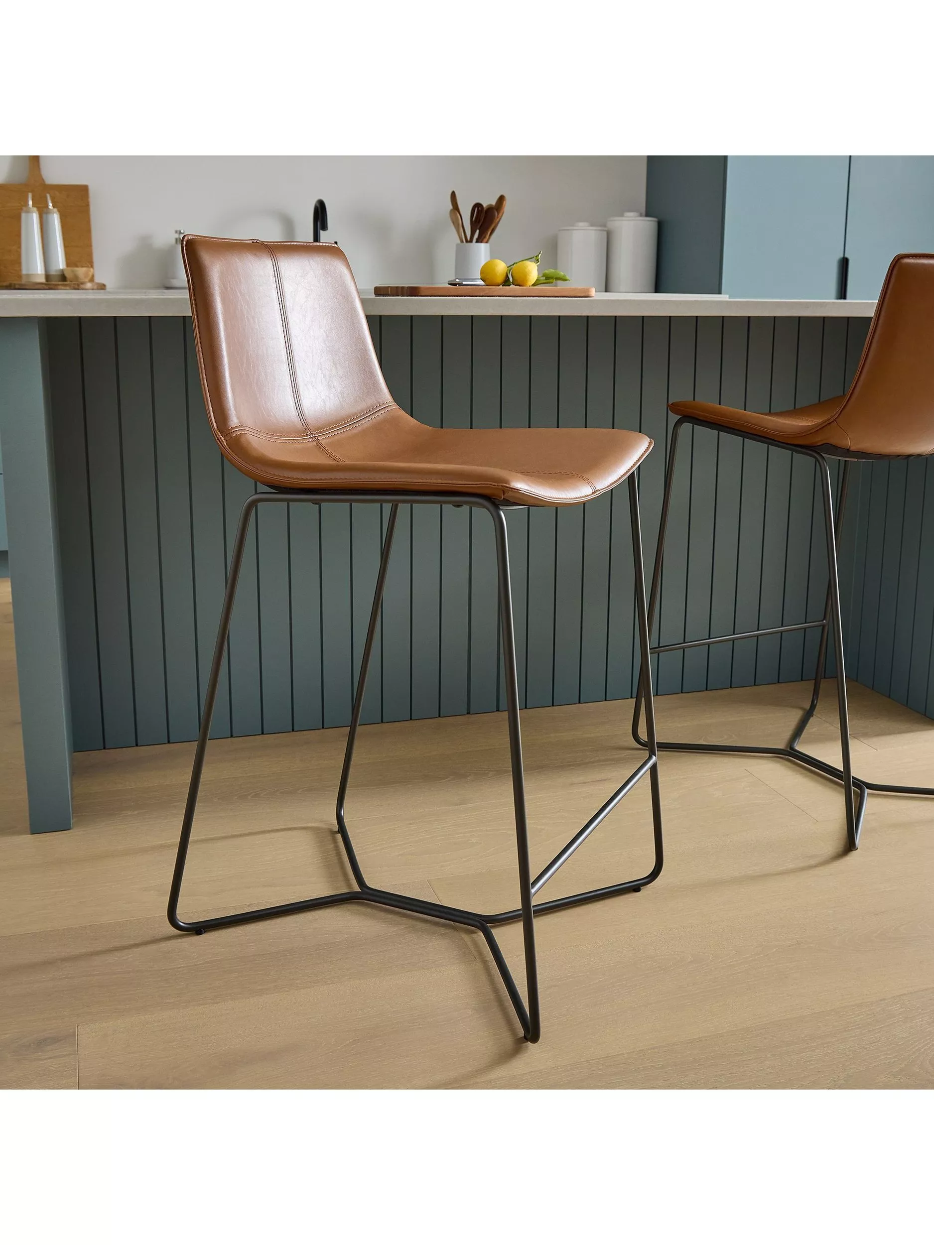 Modern tan leather bar stool with black metal legs in a contemporary kitchen with island and wooden floor