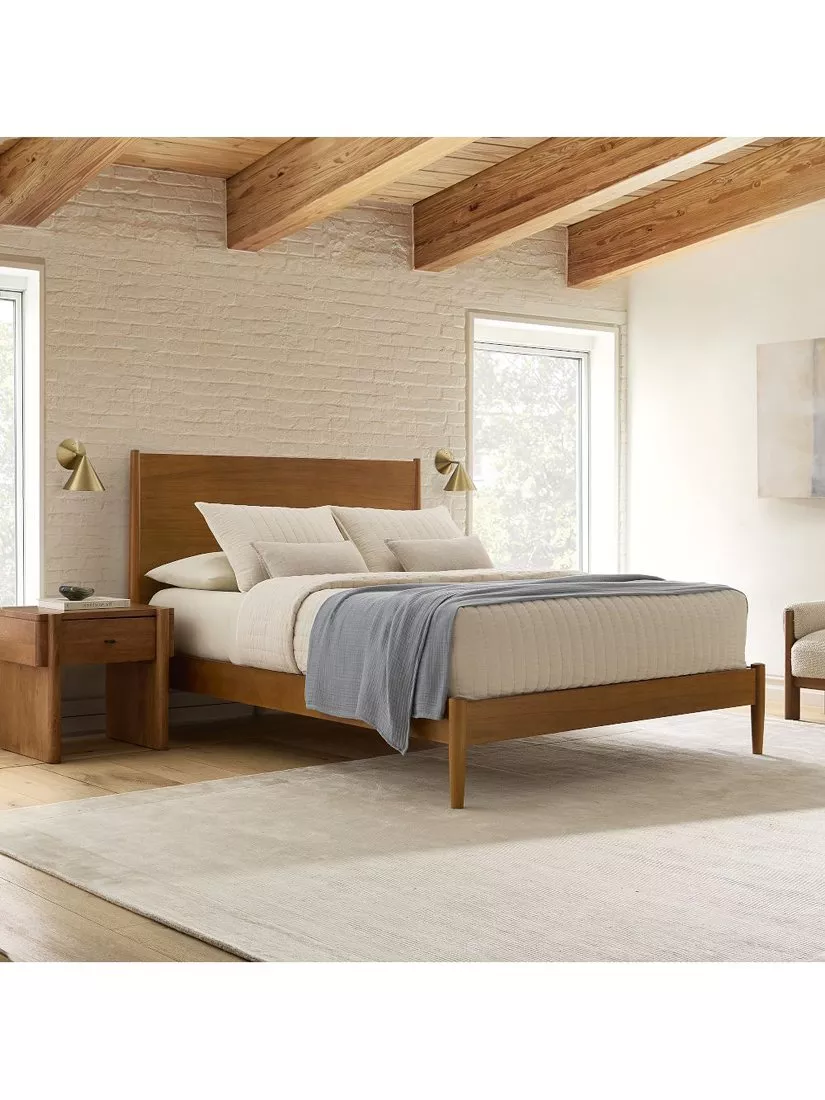 Modern wooden bed frame in bright bedroom with white brick wall, exposed beams, bedside tables and lamps