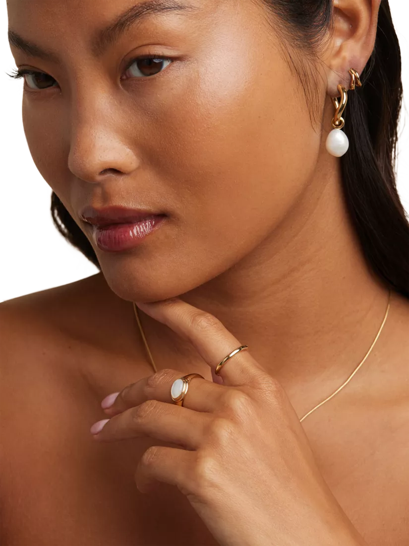Person wearing a silver chain, pearl earrings and a matching pearl ring