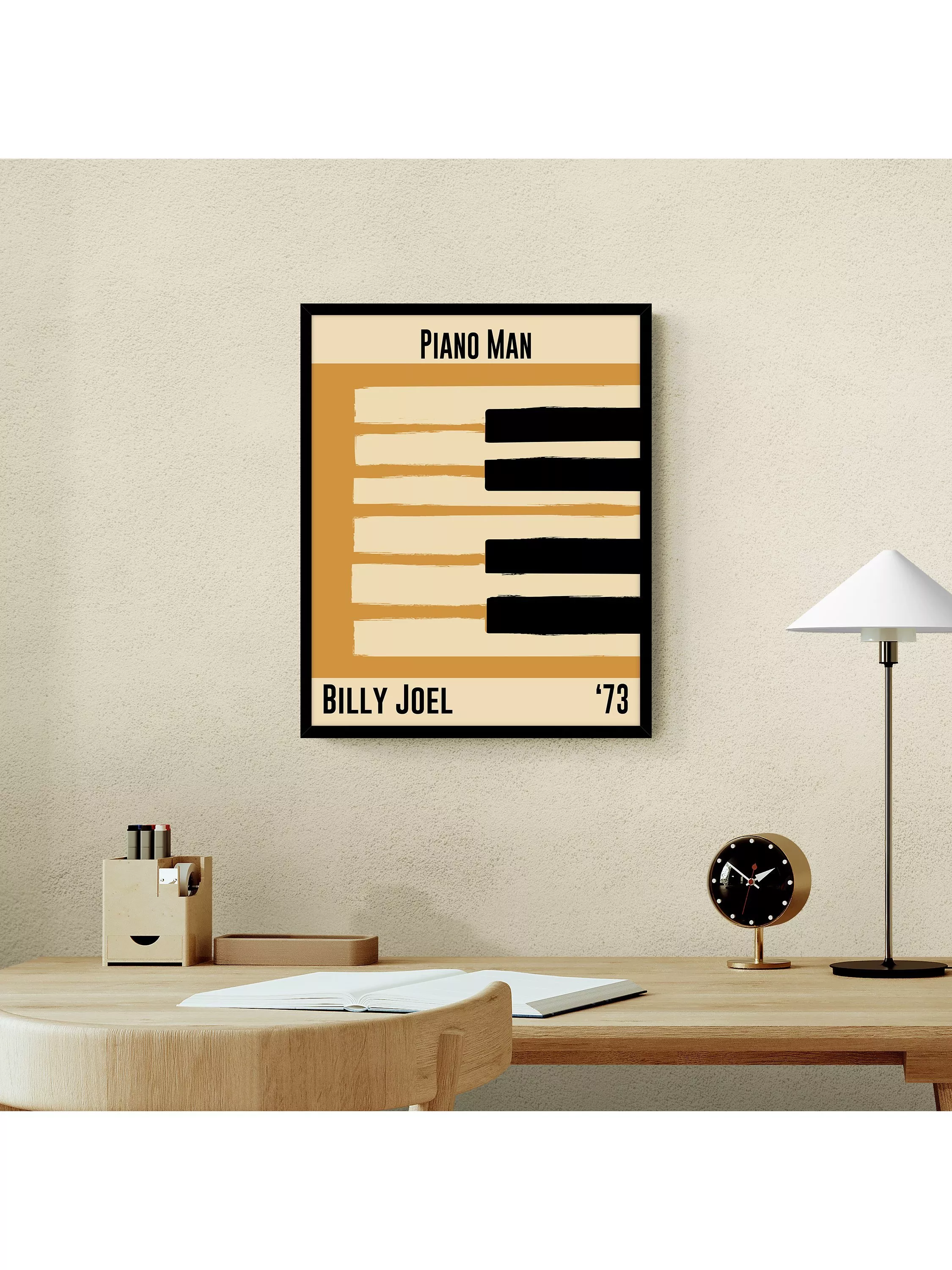 Framed Piano Man Billy Joel ’73 piano keys poster above wooden desk with lamp, clock and stationery in home office