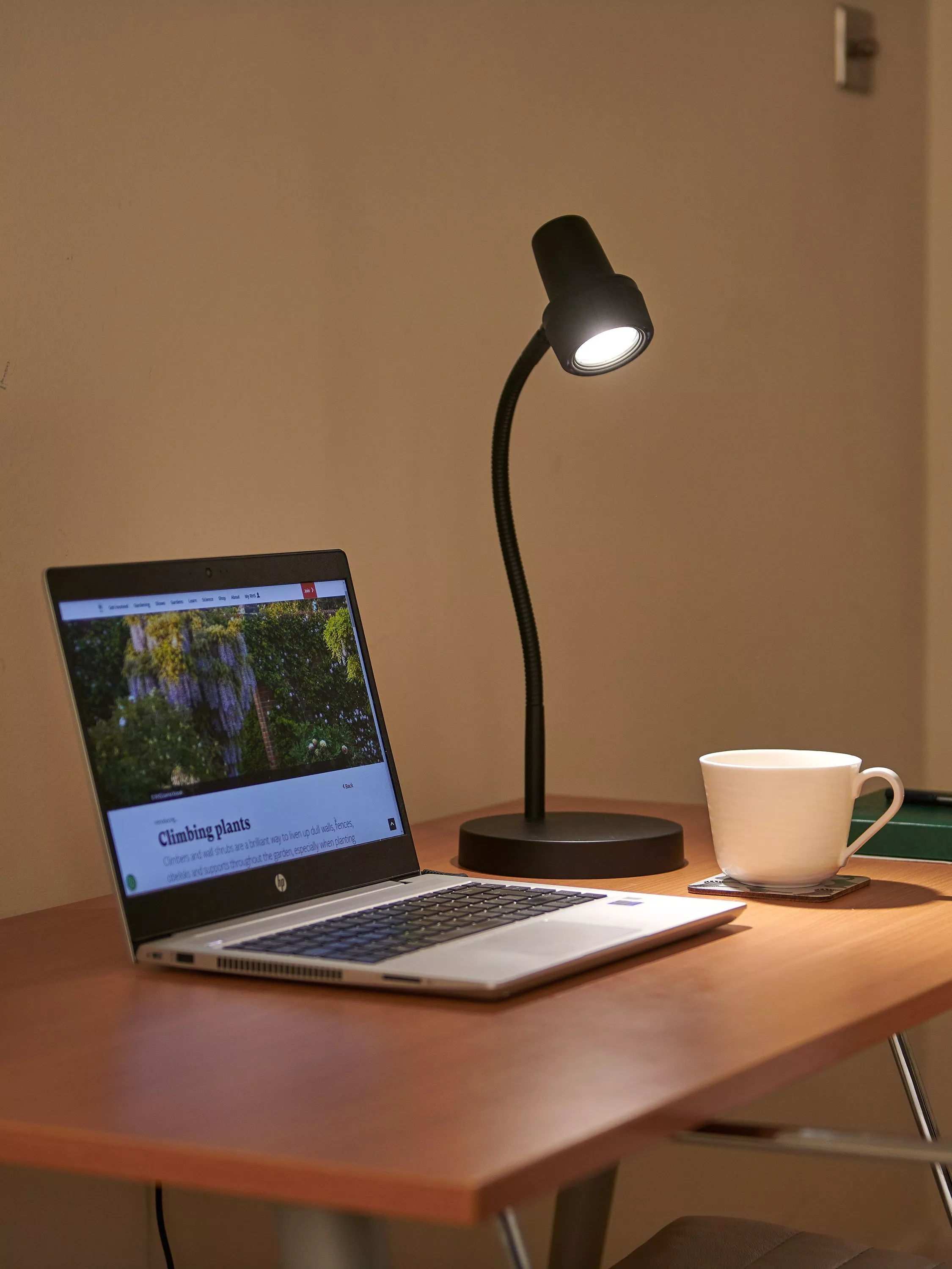 Home office desk setup with laptop, LED desk lamp and white mug, creating a warm workspace scene.