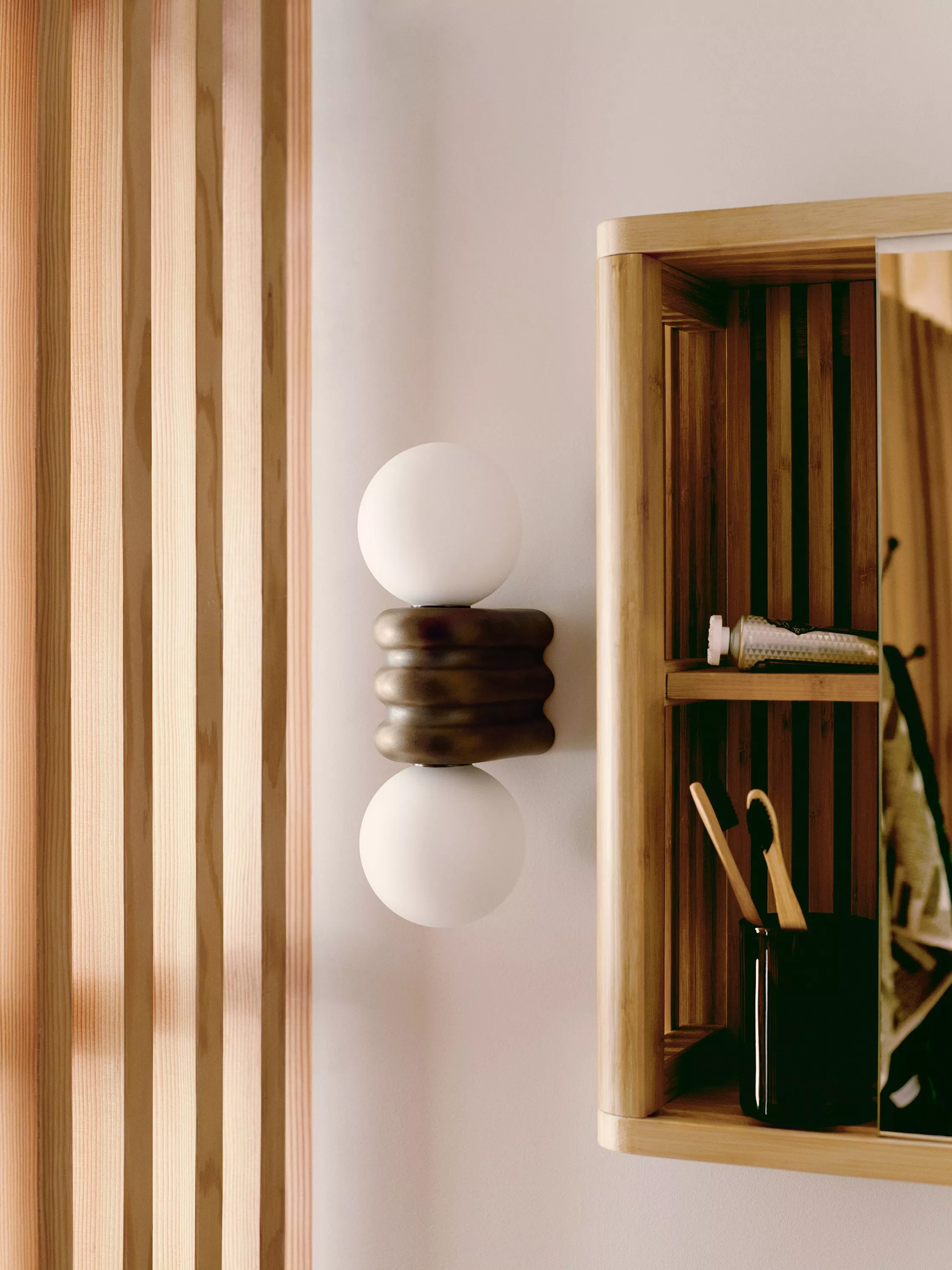 Modern bathroom wall sconce with twin frosted globes beside wooden slat panelling and shelf unit