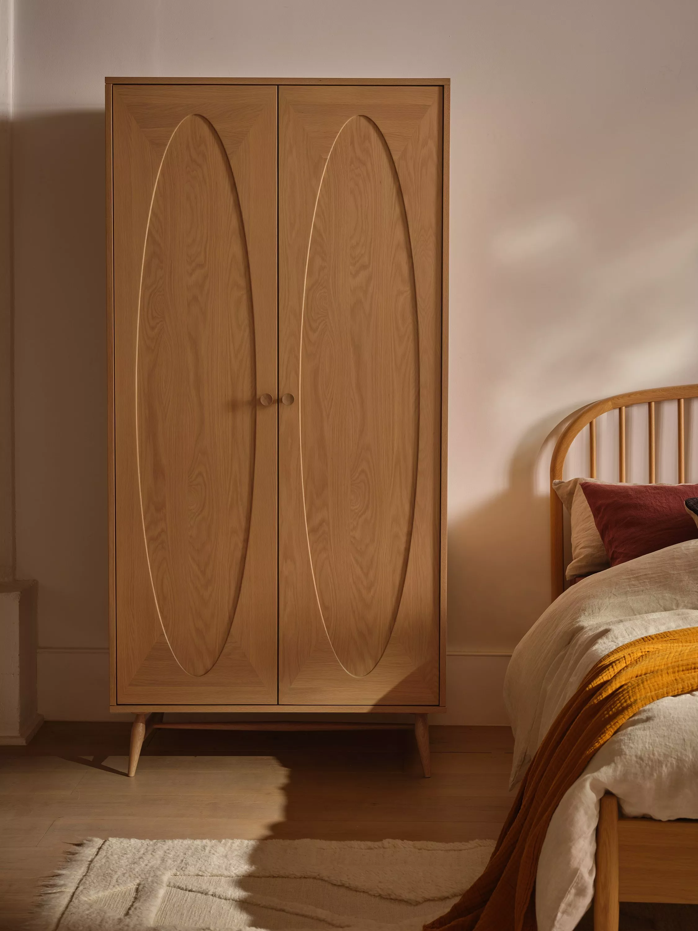 Black rattan wardrobe with open doors showing floral dresses on hangers in a stylish bedroom interior setting